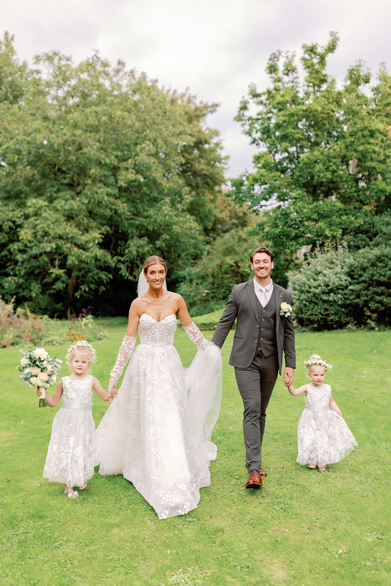 A wedding party walks together on lush green grass with trees in the background.