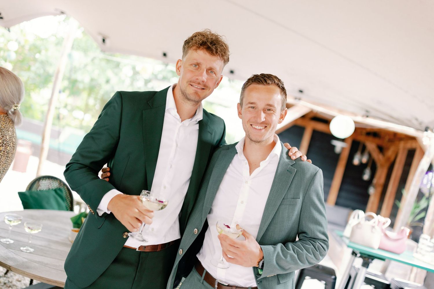 Two people in formal attire share a laugh while holding beverages at an outdoor event.