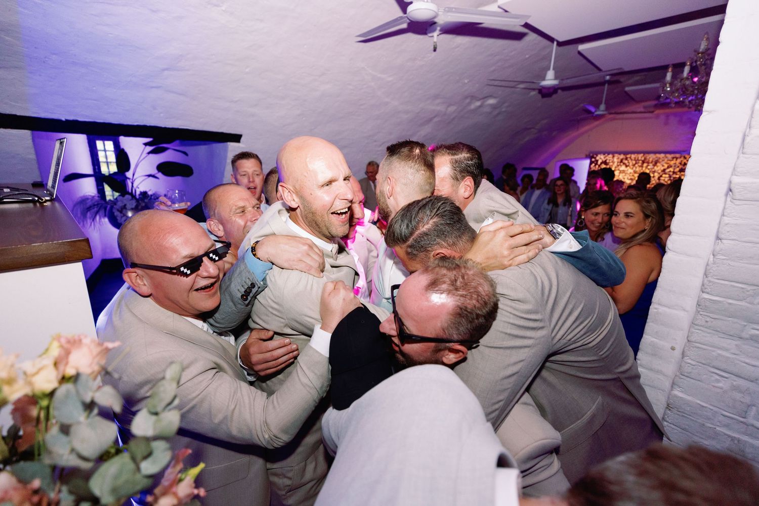 A sequence of candid dance floor moments at a wedding reception with purple lighting and white walls.