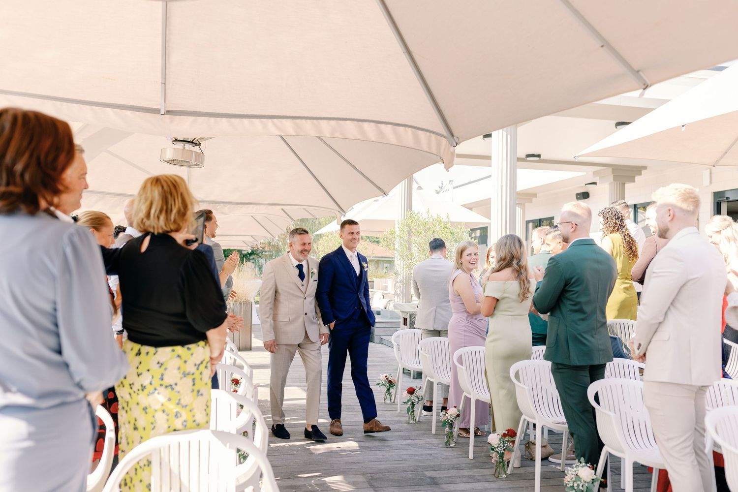 Wedding guests gathering under a covered outdoor venue with white chairs.