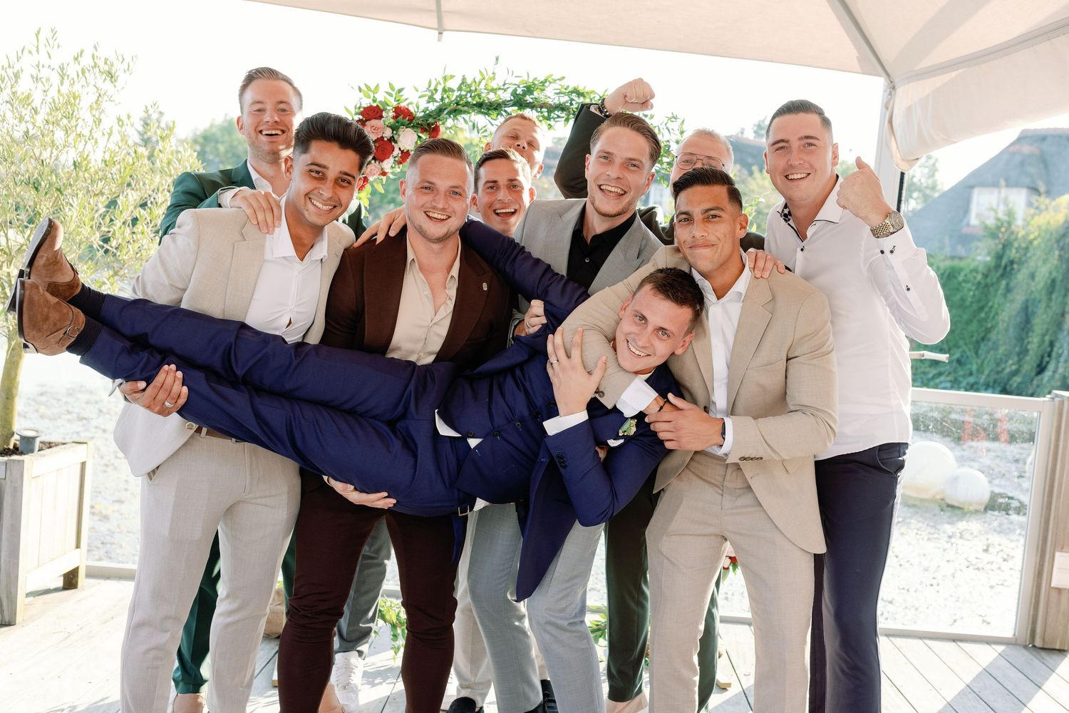 Groomsmen in navy suits and white shirts pose playfully on wooden deck.