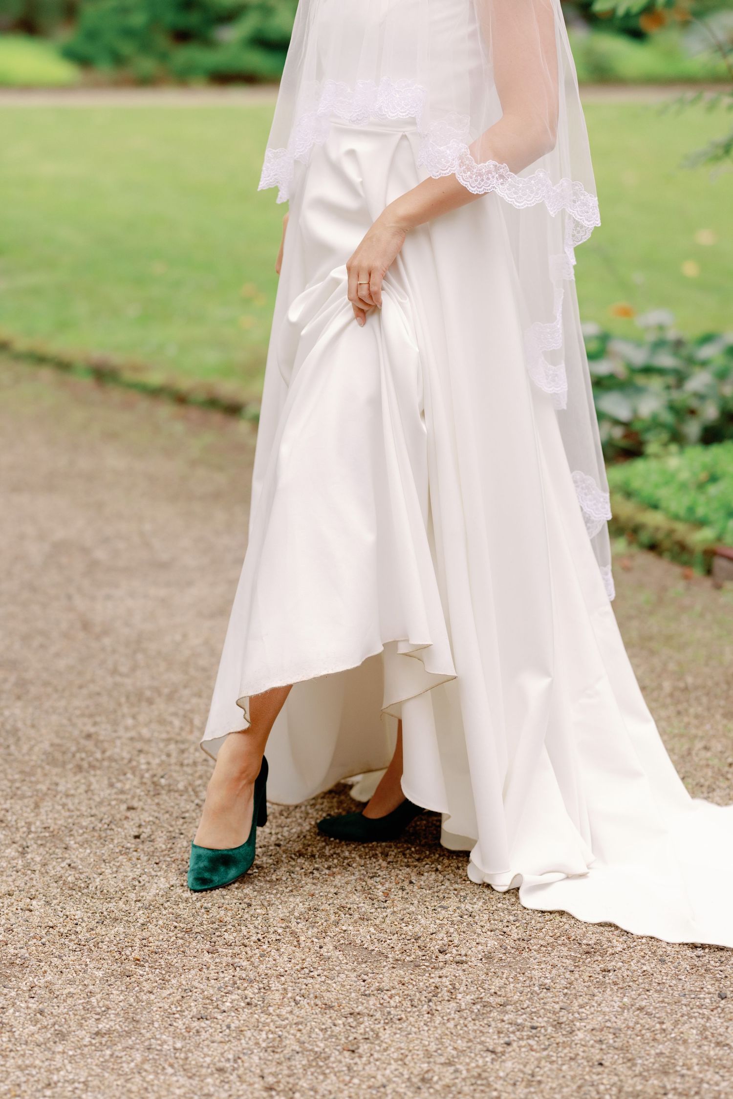 Close-up of white wedding dress hem and shoes on a gravel pathway.