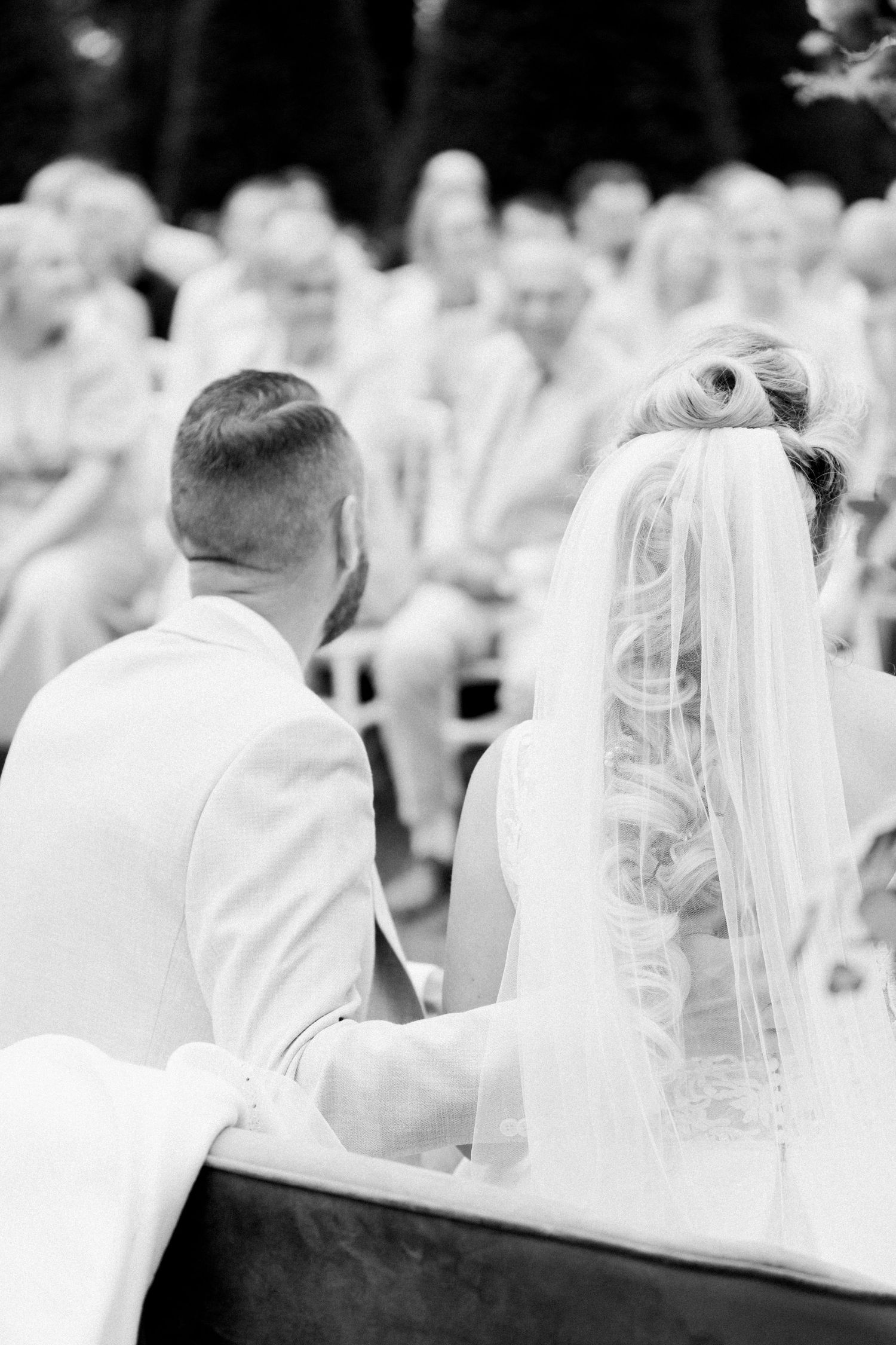 A black and white wedding photograph showing a couple seated together during their ceremony.