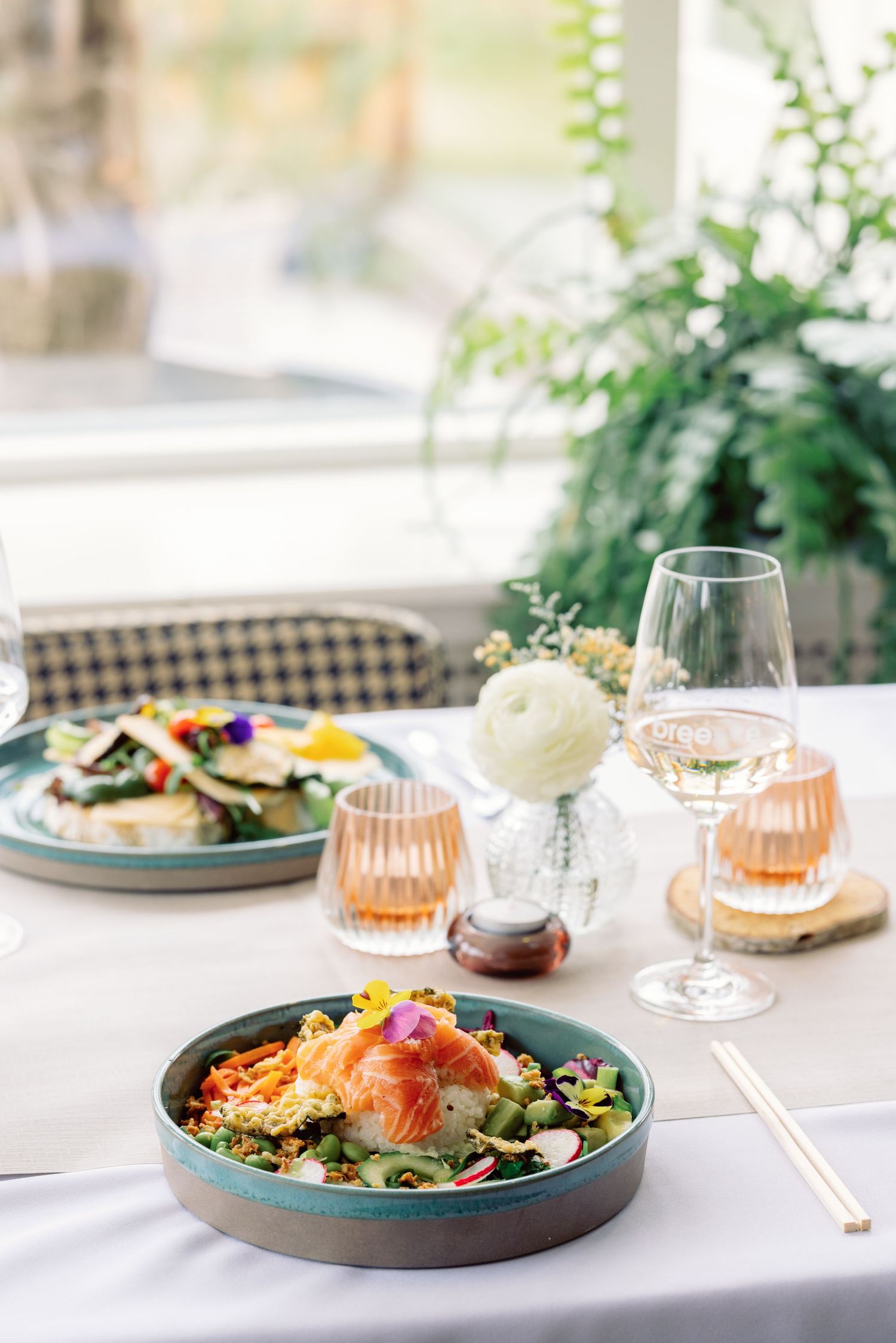 Three elegant table settings with colorful salads, wine glasses, and soft lighting create an upscale dining atmosphere.