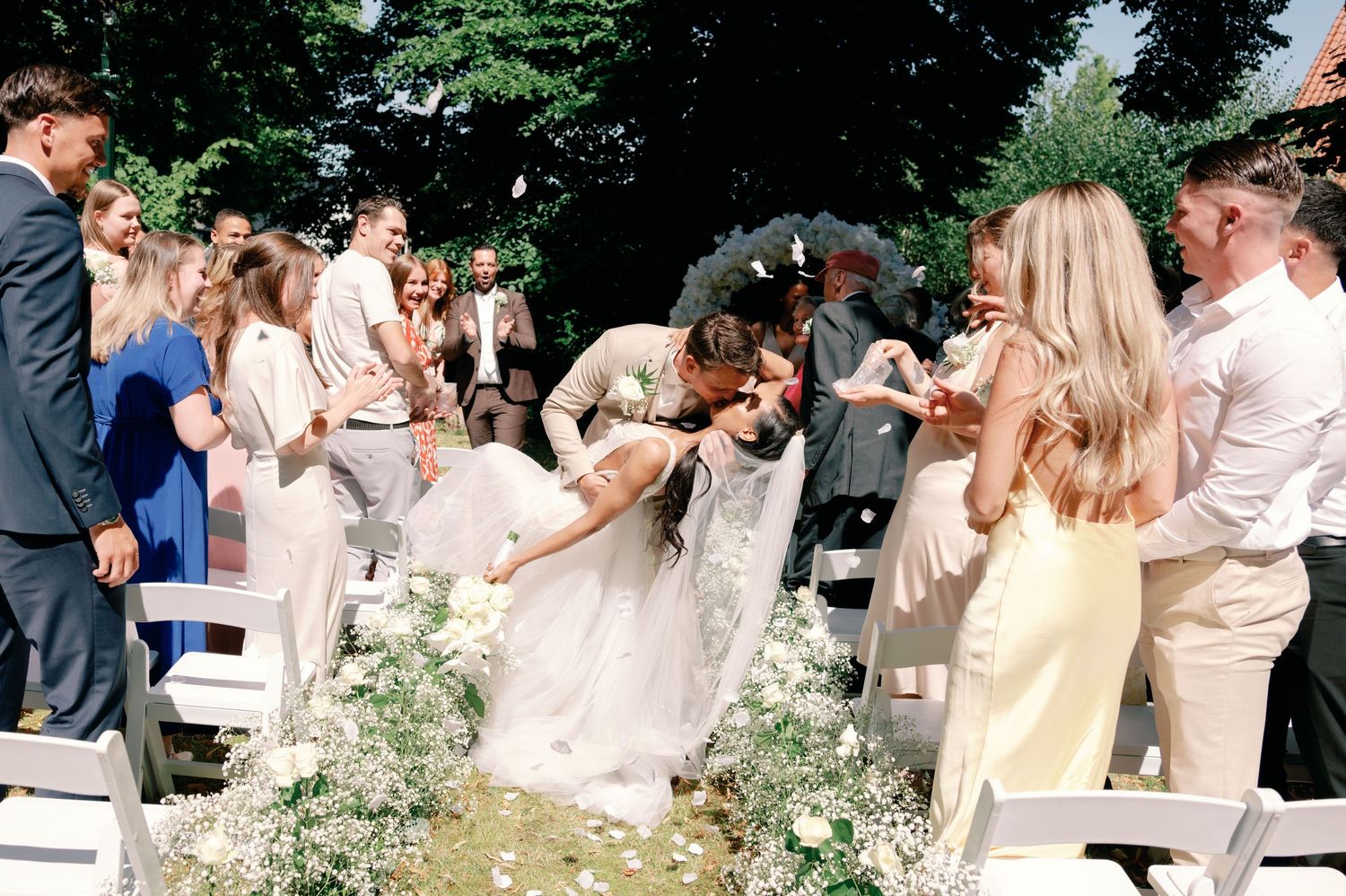A group of wedding guests celebrate outdoors in an elegant garden setting with greenery and floral decorations.