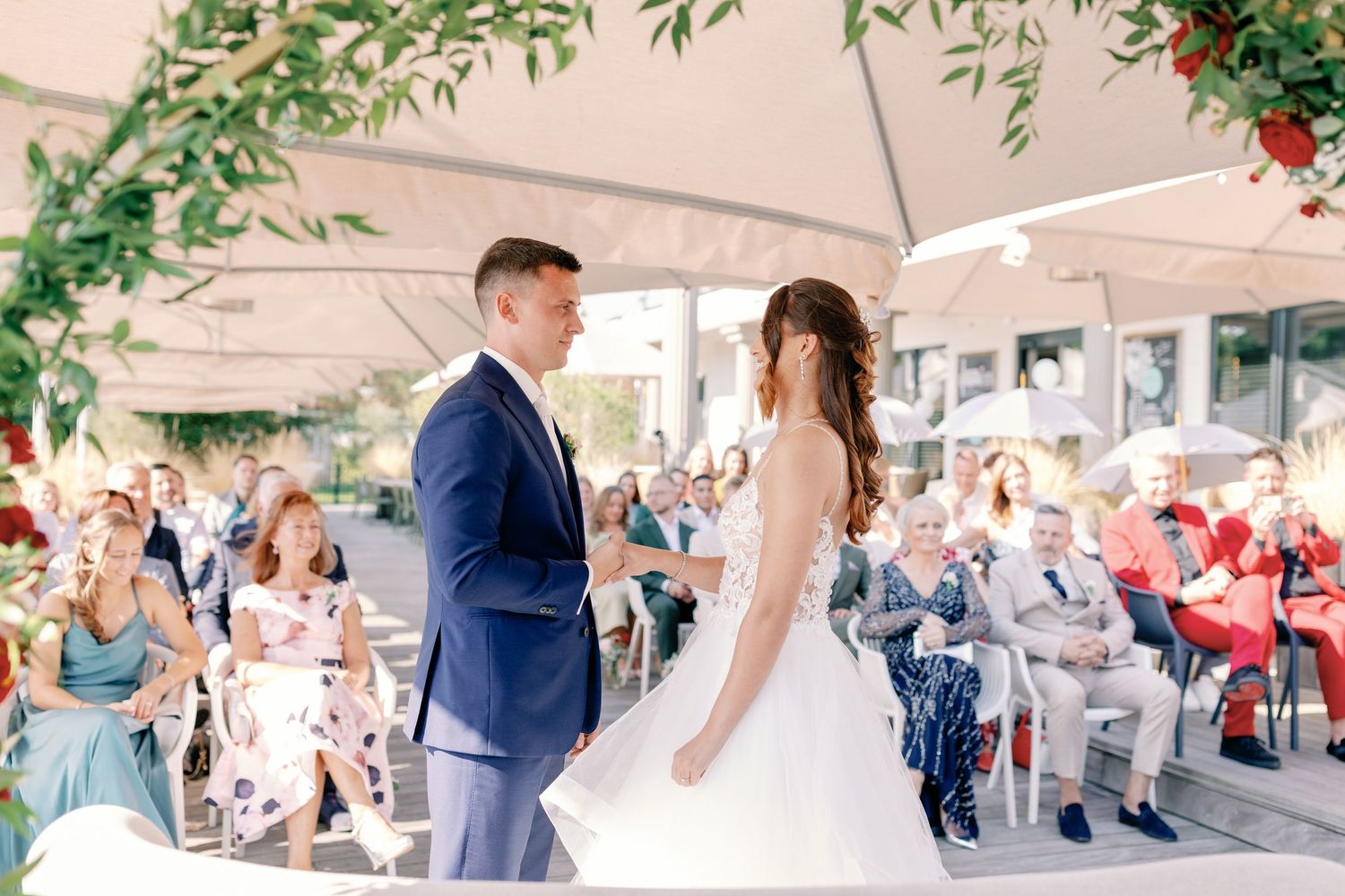 An outdoor wedding ceremony with guests watching as the couple exchanges vows under a white canopy.