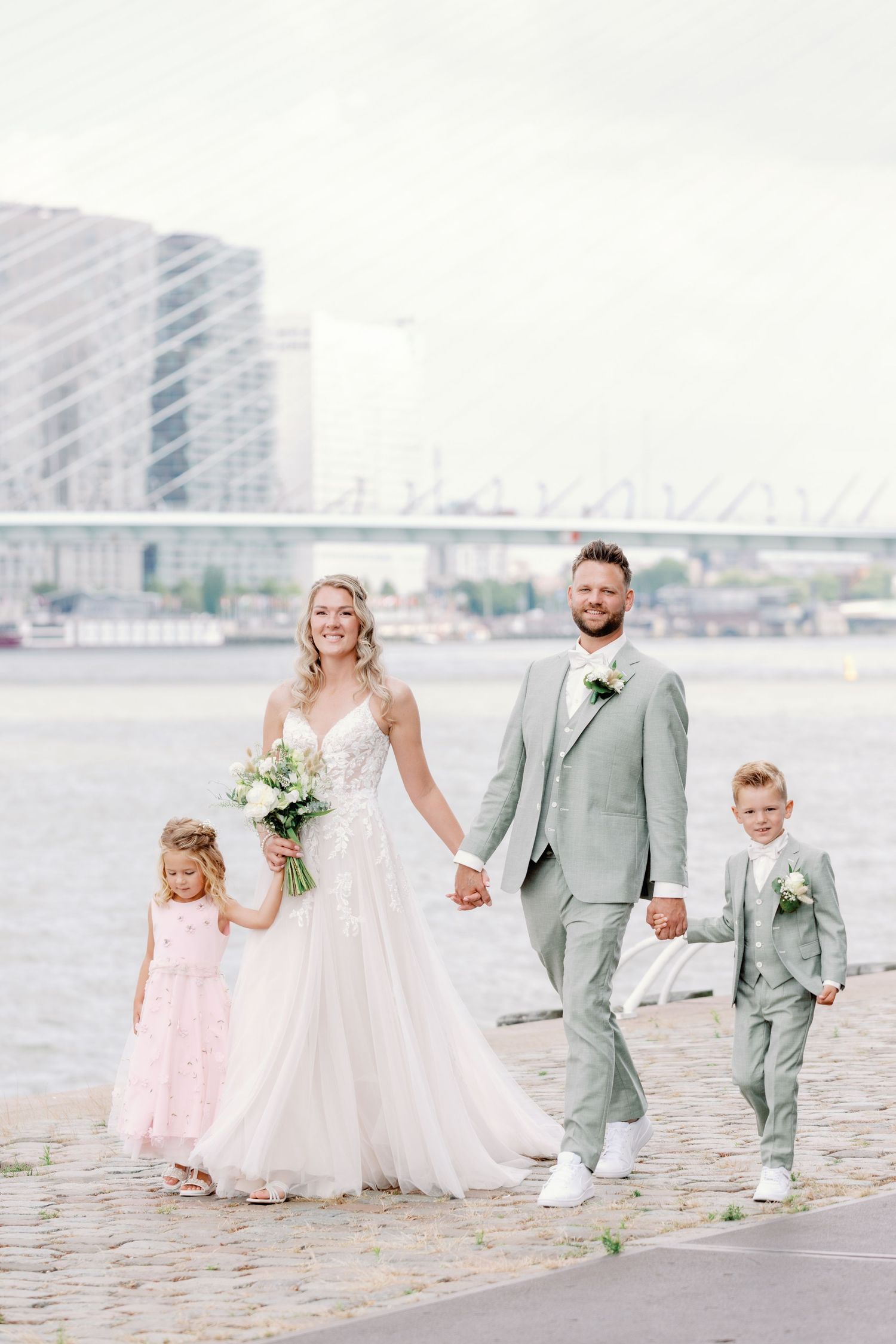Wedding party poses on beach with city skyline in background wearing pink and gray attire.