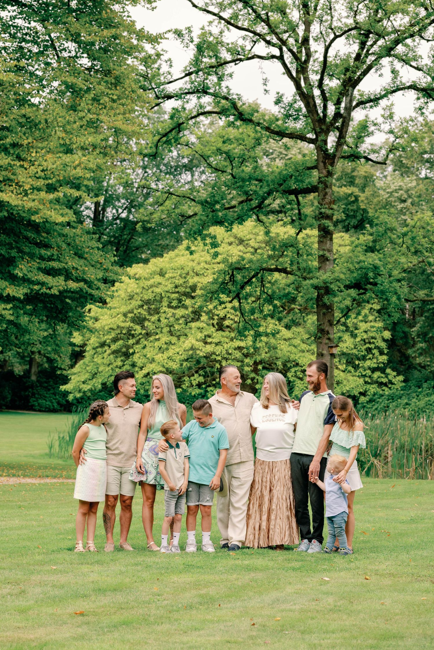 Group photo session in a lush green park with people wearing coordinated light-colored outfits.