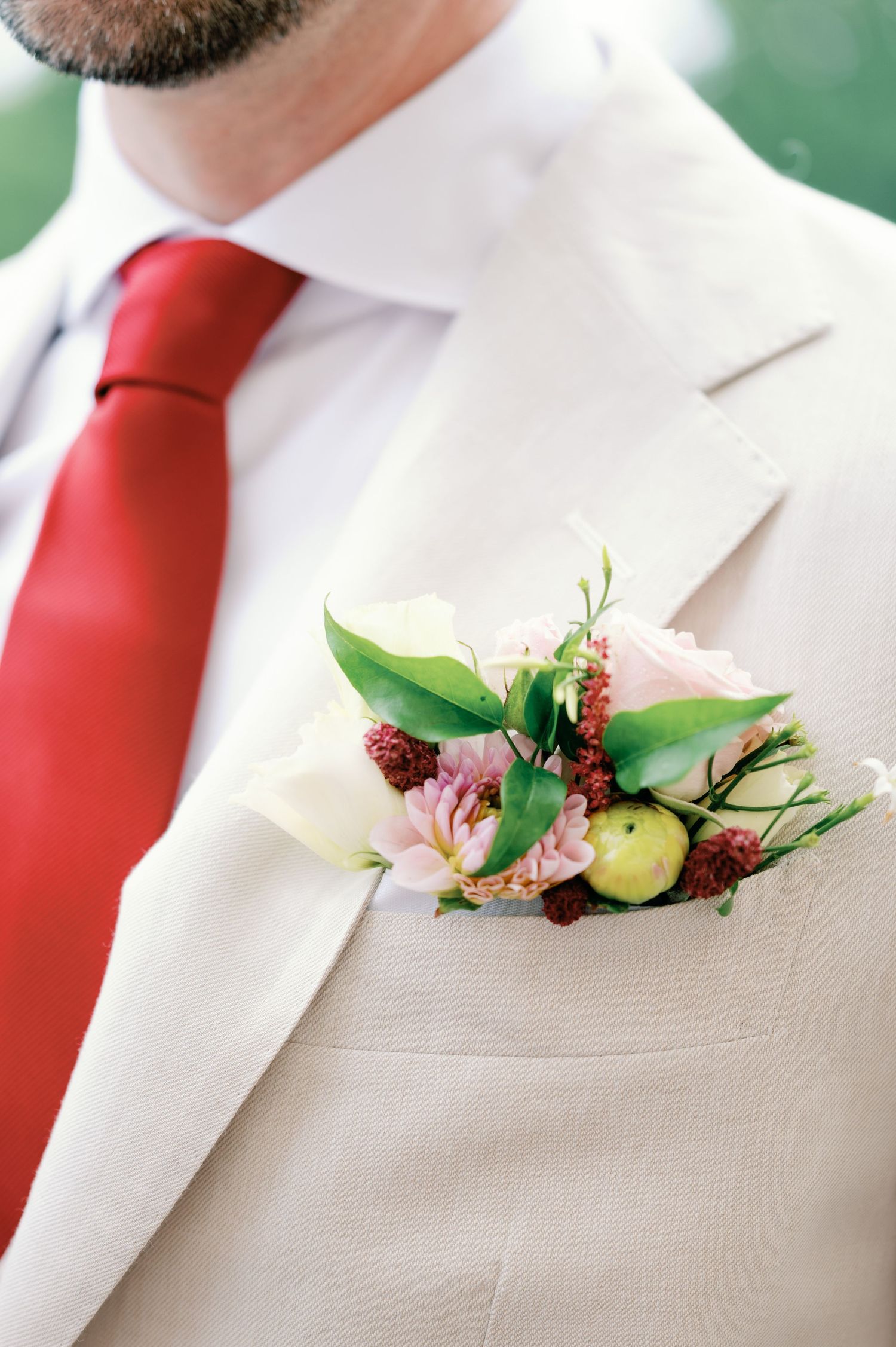 Close-up view of groomsmen wearing beige suits with red ties and floral boutonnieres at a wedding.