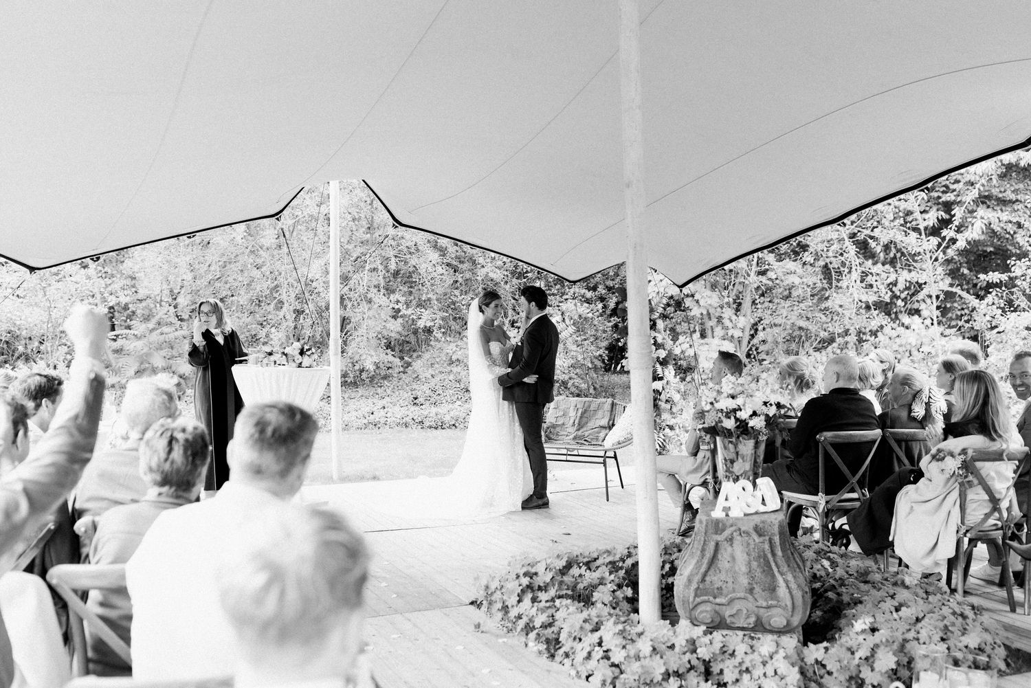 A black and white panoramic photograph shows a crowd gathered outdoors at a social event in a scenic setting.