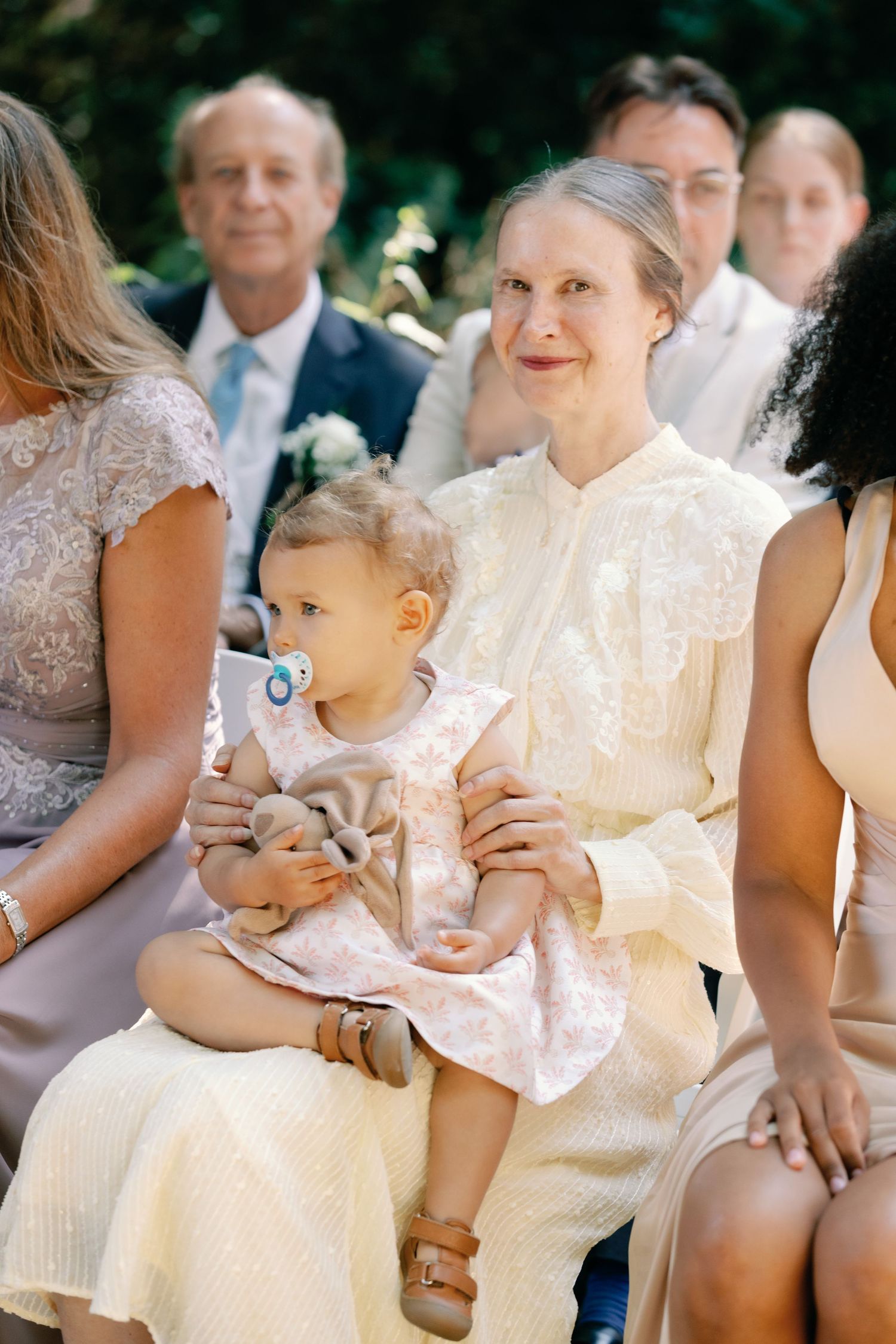 A gathering at an outdoor event shows attendees in white attire with a small child sitting on someone's lap.