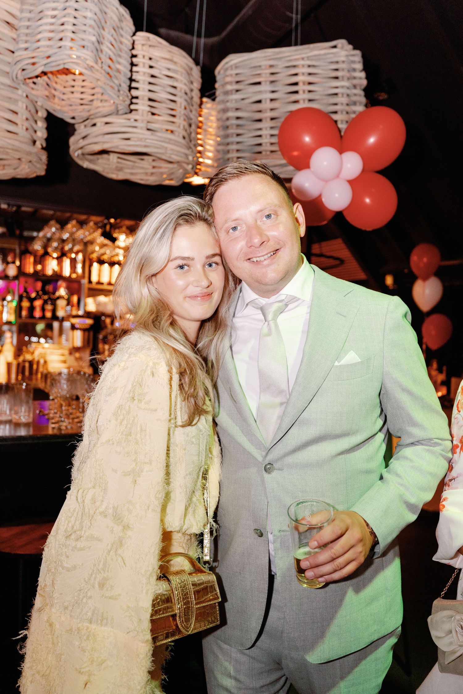 A couple shares a sweet moment together at a party venue decorated with pink and red balloons.
