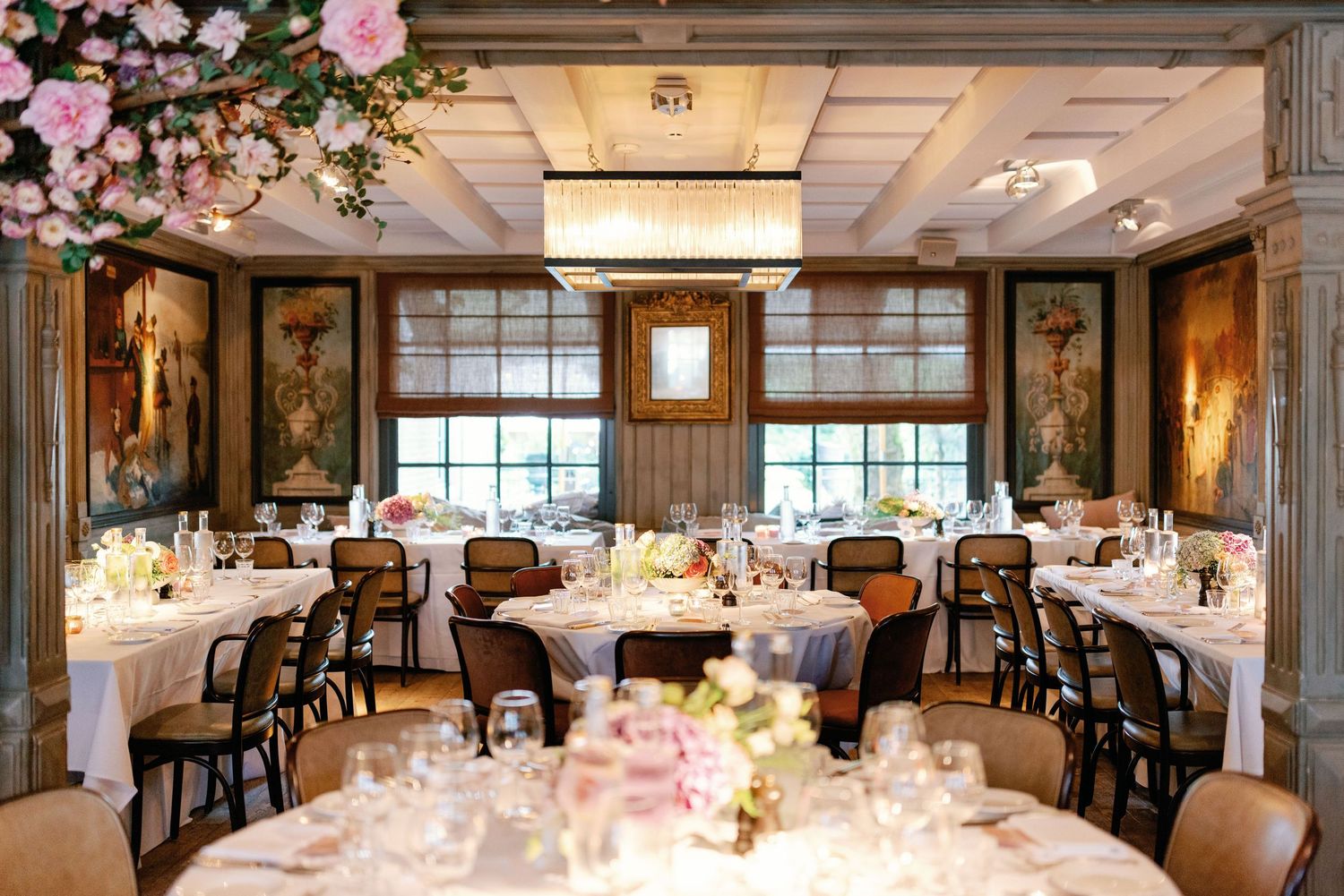 Elegant wedding reception venue with round tables, pink floral centerpieces, and crystal chandeliers in a grand ballroom.