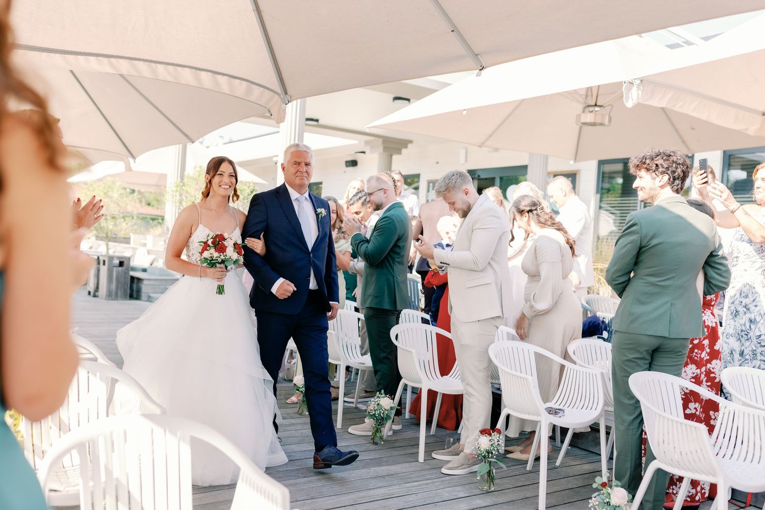 Wedding guests seated in white chairs under a tent during an outdoor ceremony.