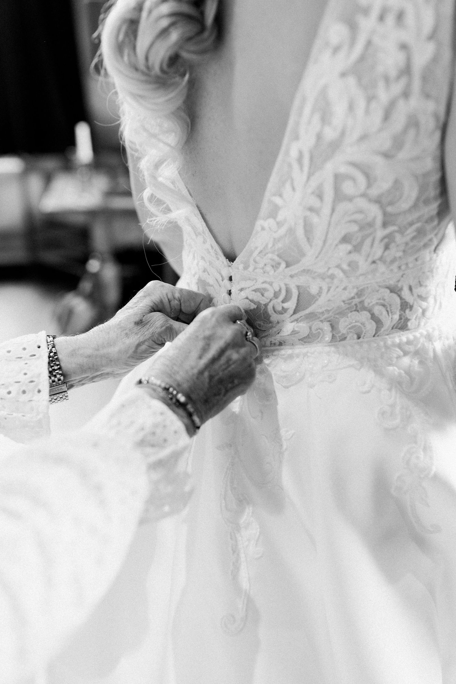 Close-up details of a white lace wedding dress being fastened with buttons down the back.