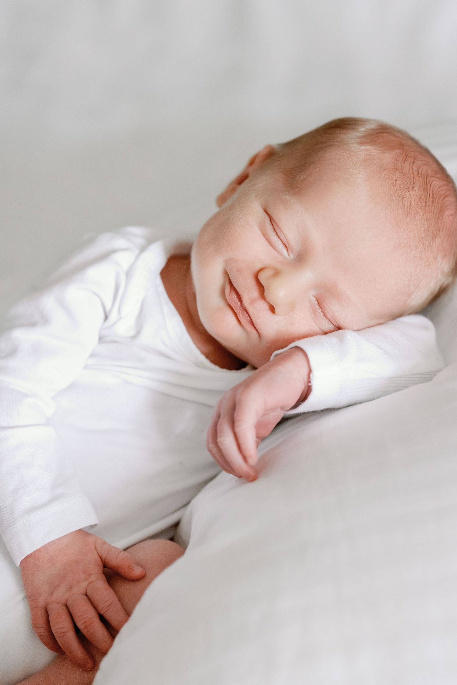 Close-up profile view of a sleeping baby in white clothing against white bedding.