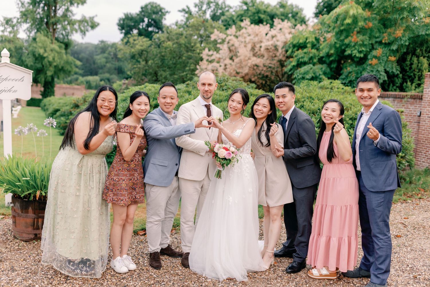 Wedding party in pastel dresses and gray suits poses outdoors in a garden setting during a summer celebration.