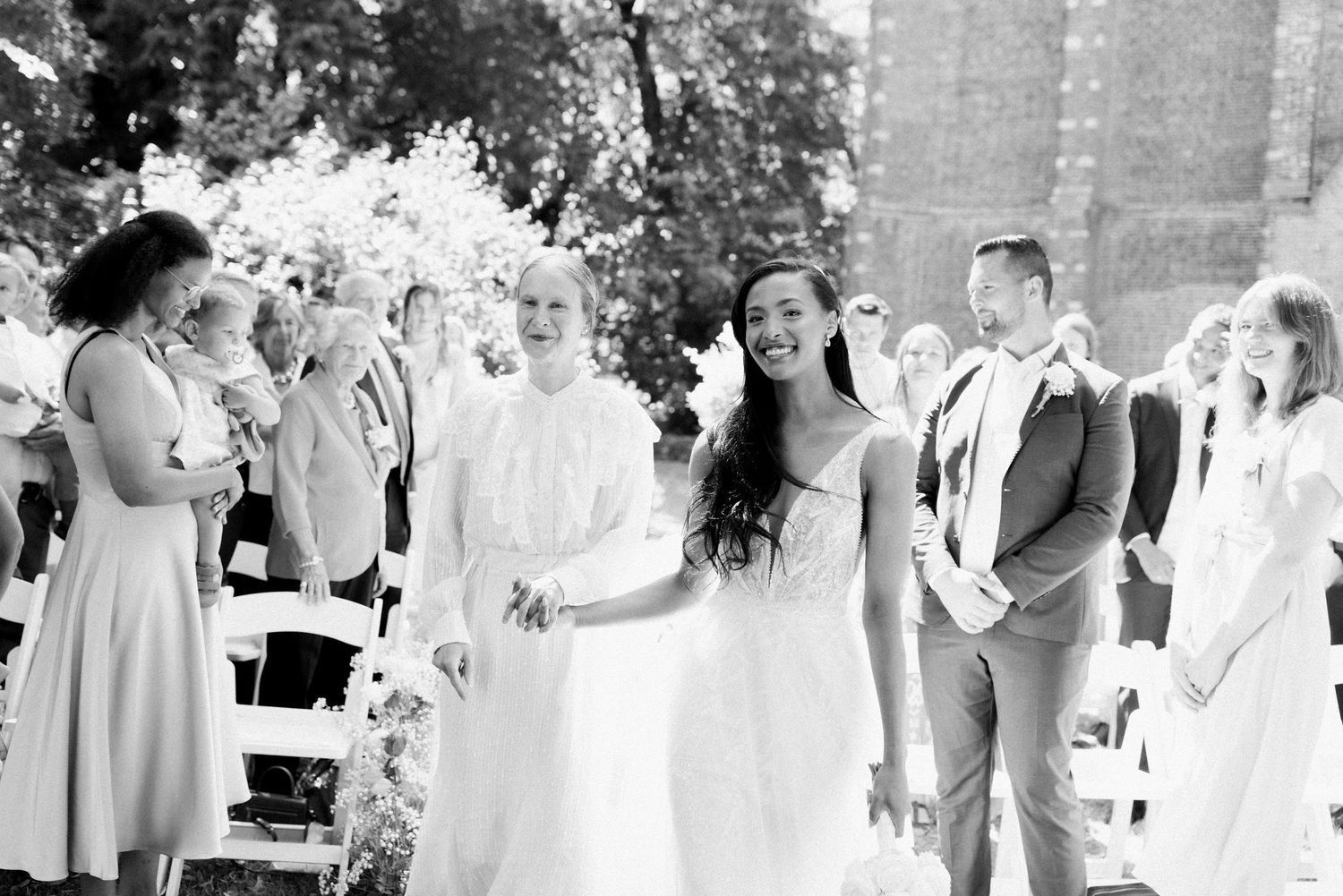 A wedding party celebrates outdoors during a summer reception with guests mingling and dancing in a garden setting.