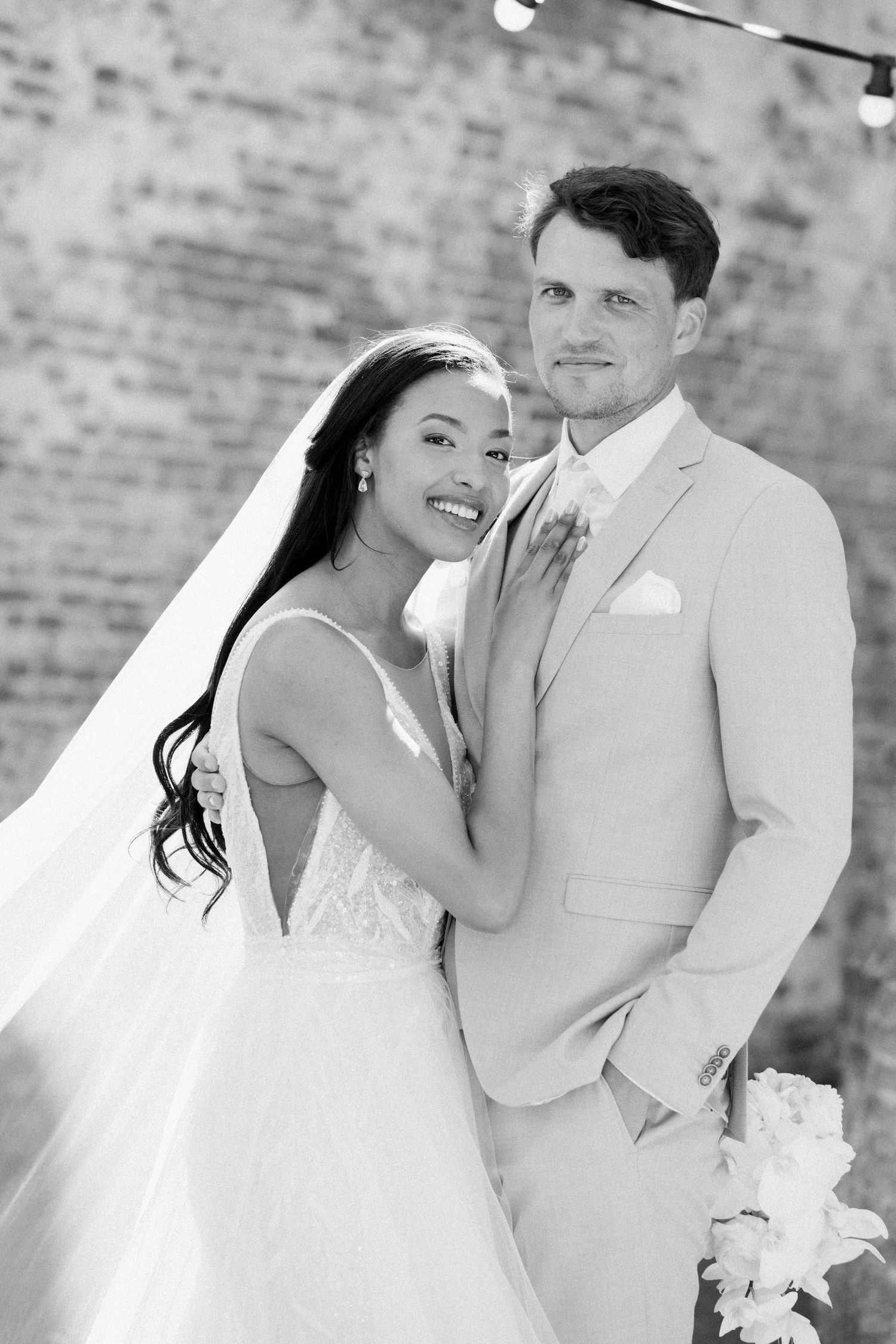 A joyful wedding couple embraces and laughs together against a brick wall backdrop in a series of candid moments.