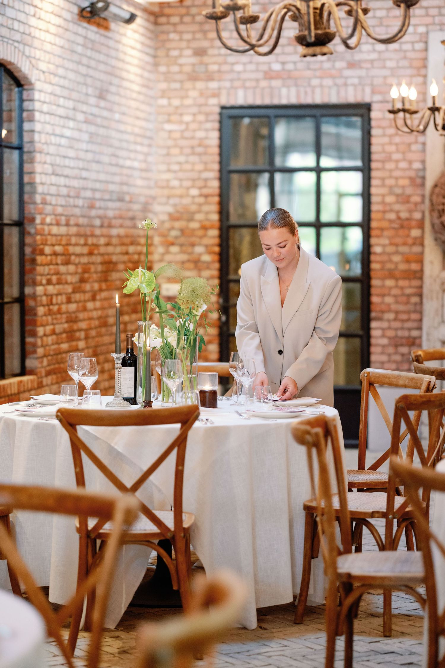 Restaurant interior with exposed brick walls, white tablecloths, and wooden chairs in an elegant dining setting.
