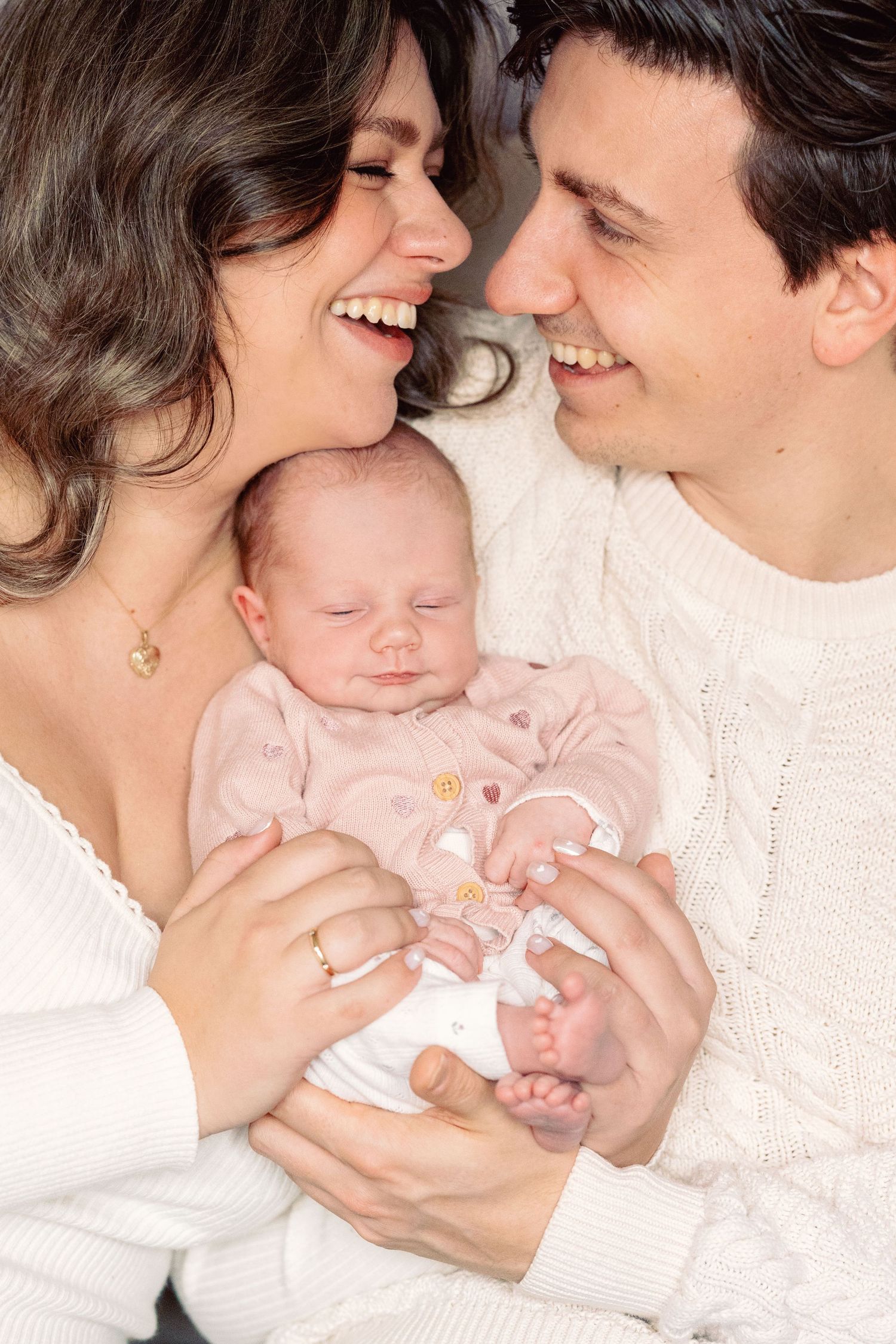 A couple in cream sweaters shares loving moments with their newborn baby.
