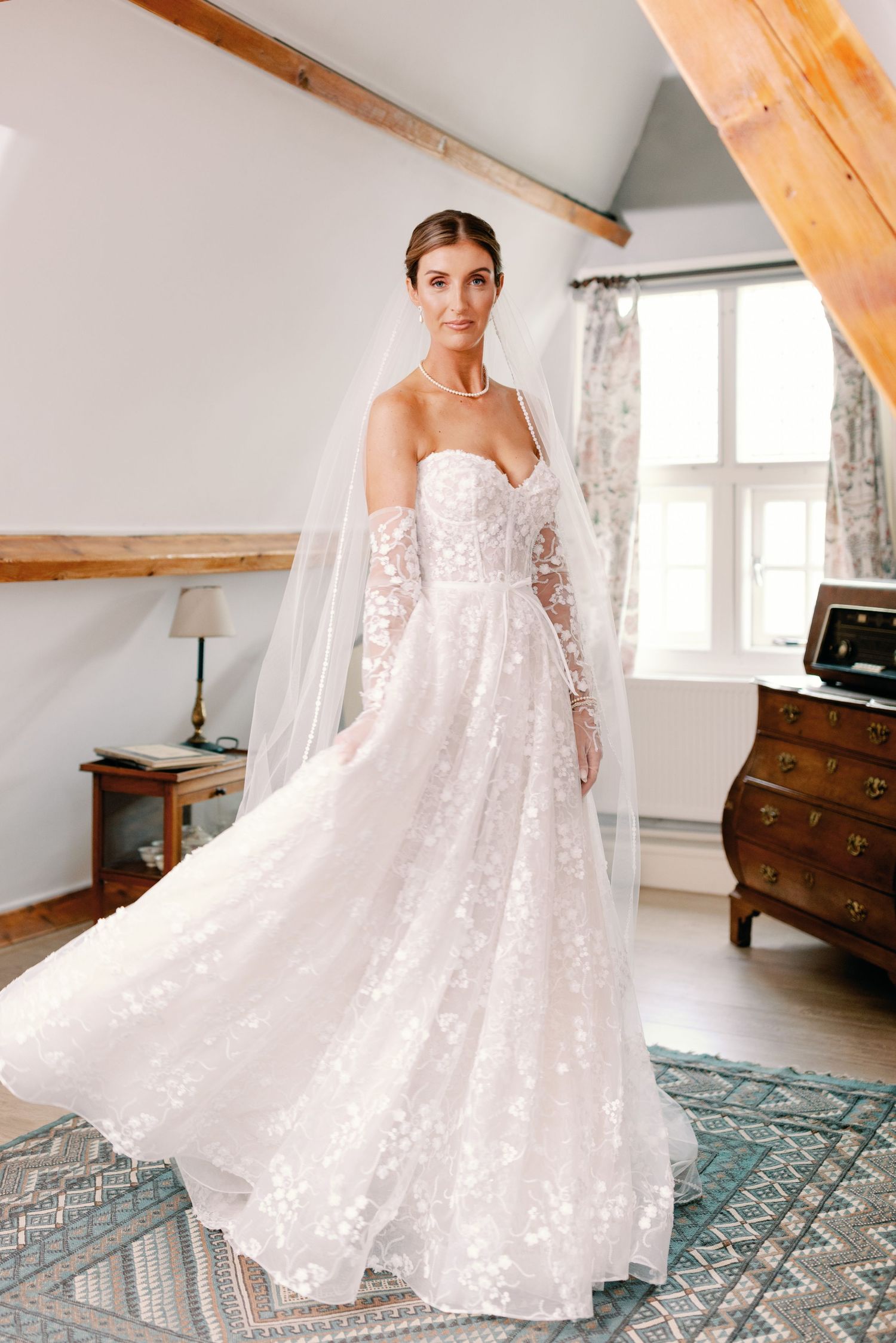Stunning lace wedding dress with long train displayed in rustic room with wooden beams.