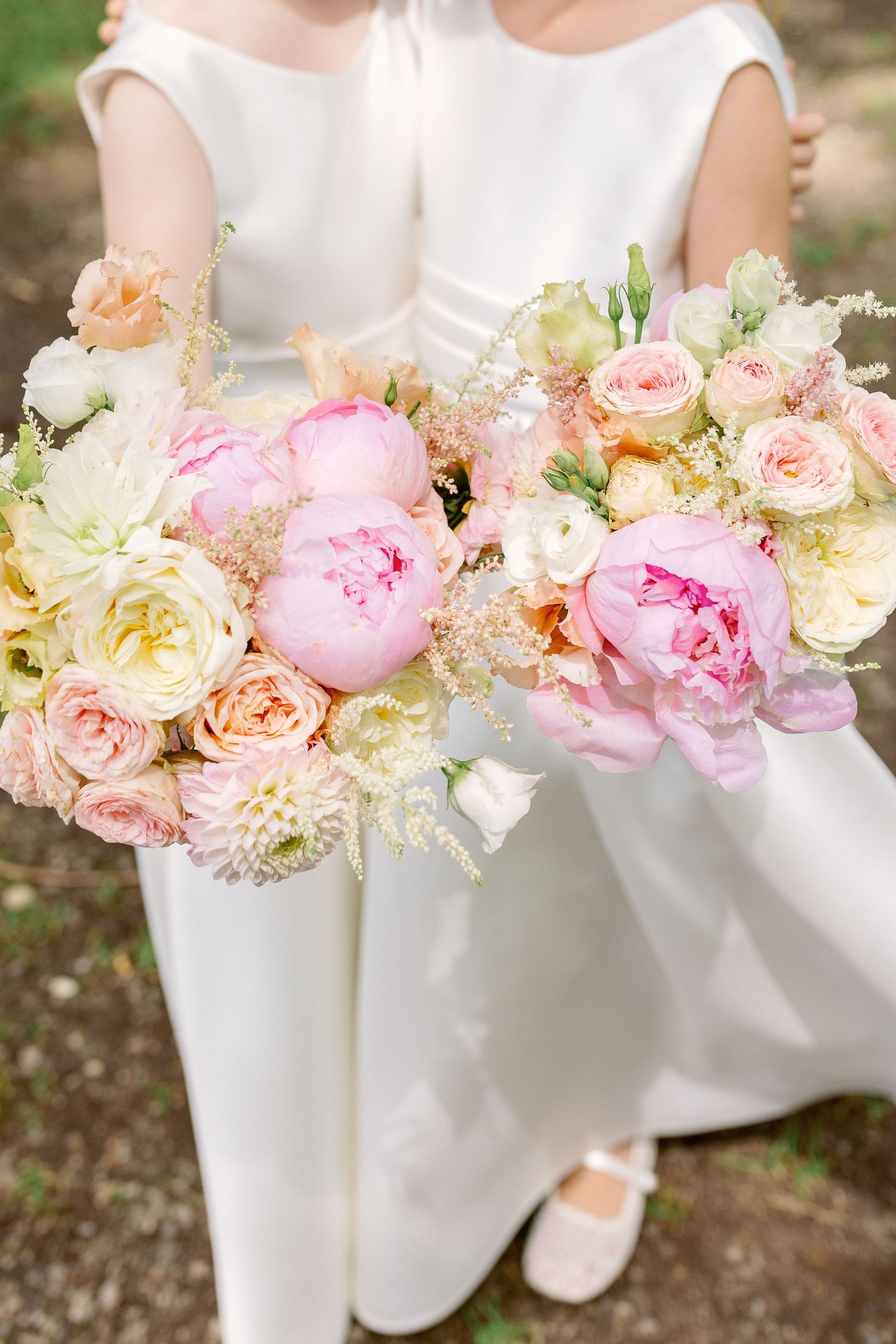 Elegant bridal party bouquets featuring pink peonies, cream roses and delicate florals against white dresses.