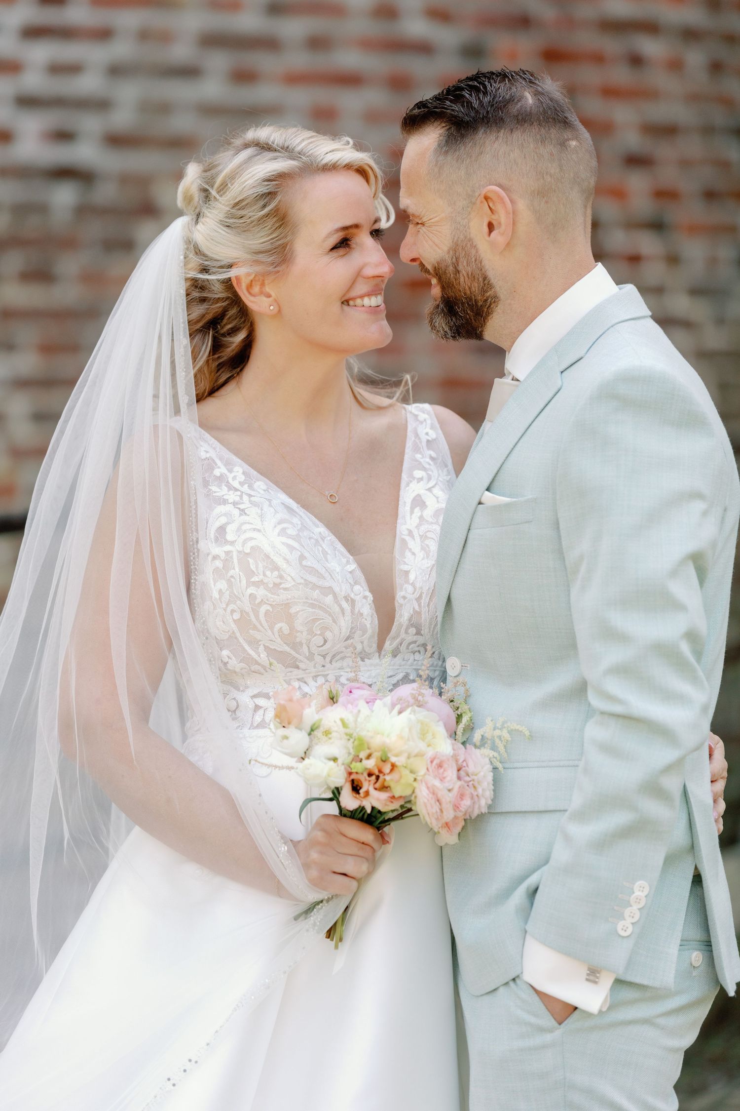 Intimate wedding portrait against brick wall with soft natural lighting.