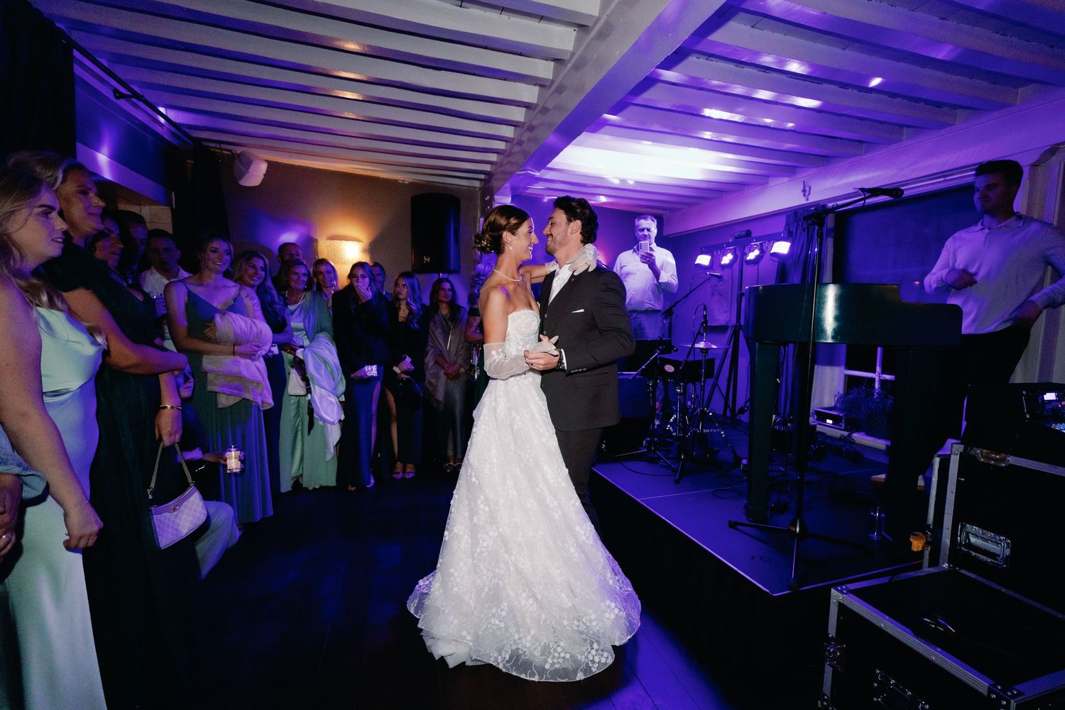 A wedding reception dance floor illuminated with purple lighting as guests dance and celebrate.
