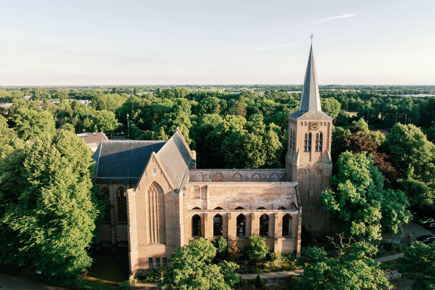 Aerial view of a historic stone church with tall spire surrounded by lush green trees in a rural setting.