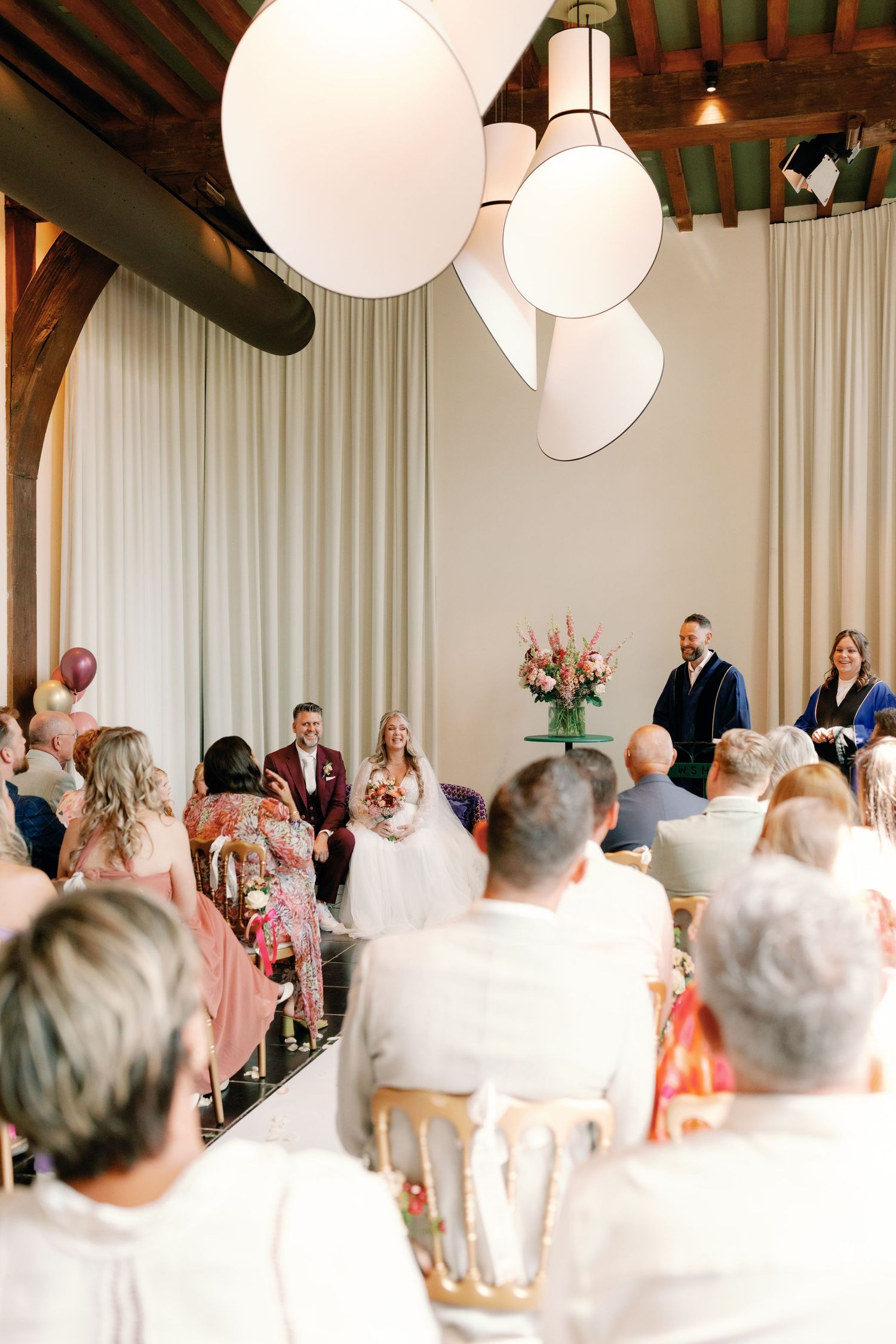 A panoramic view of a wedding reception venue with white paper lanterns and exposed wooden beams overhead.
