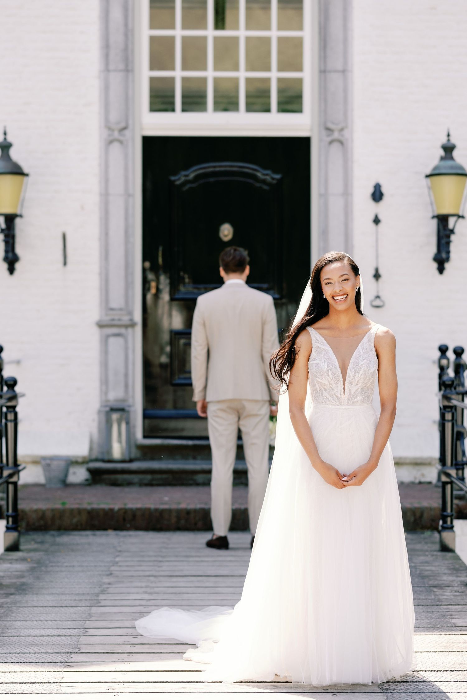 A bride in an elegant white wedding dress poses in front of a classic white building with columns.