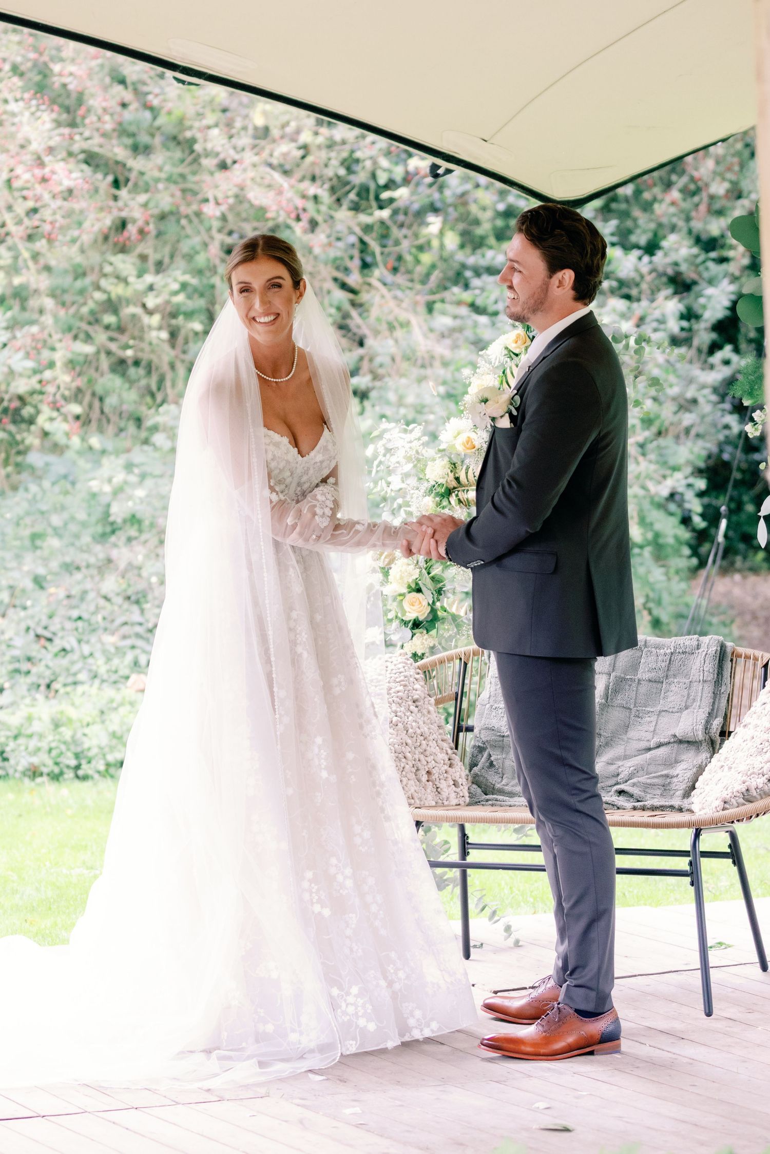 A couple shares a tender moment during their first dance at an outdoor wedding reception on a covered patio.