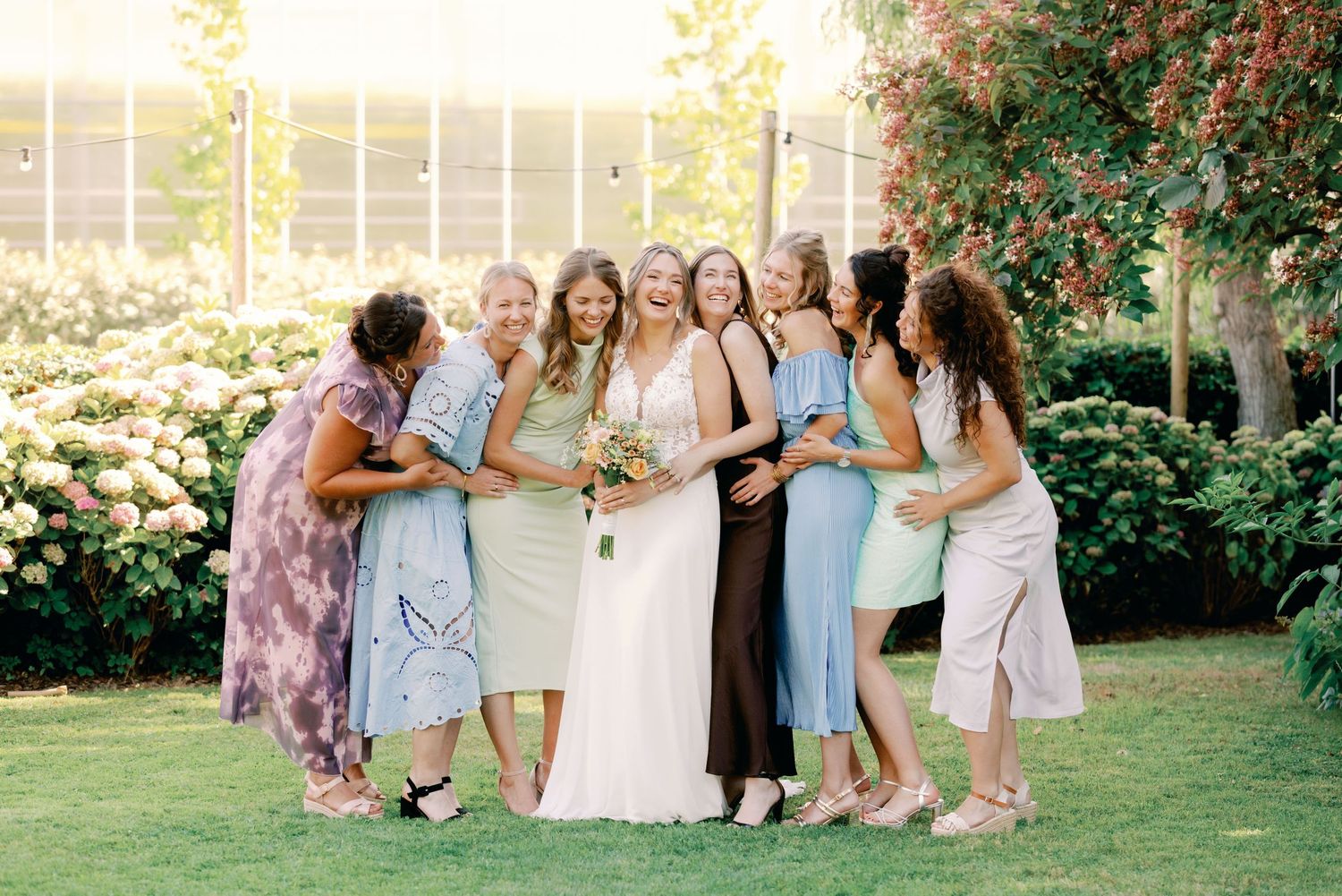 A group of people in pastel dresses pose together outdoors during a wedding celebration.