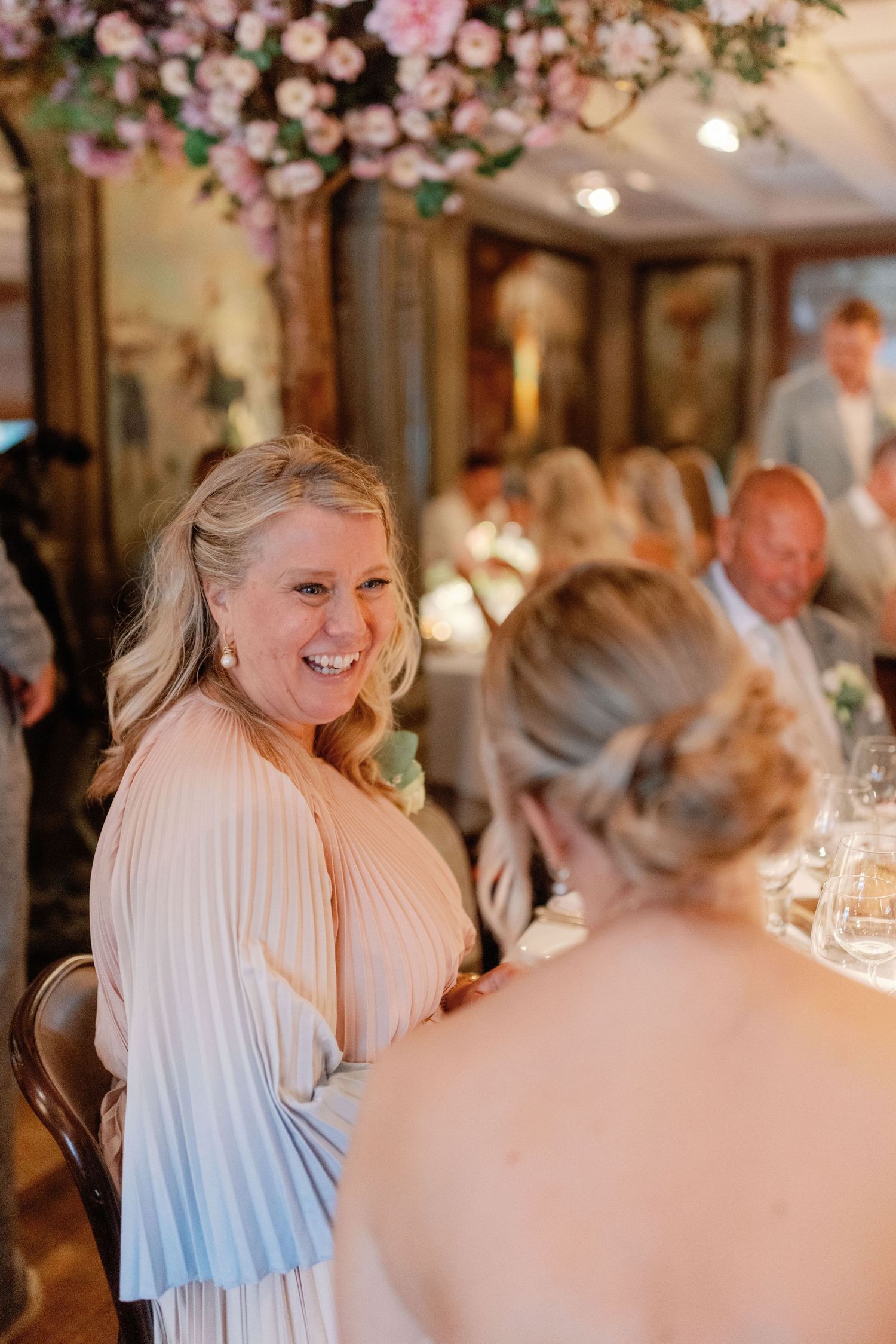 Elegant wedding reception with pink floral decor and guests dining at tables in an intimate indoor venue.