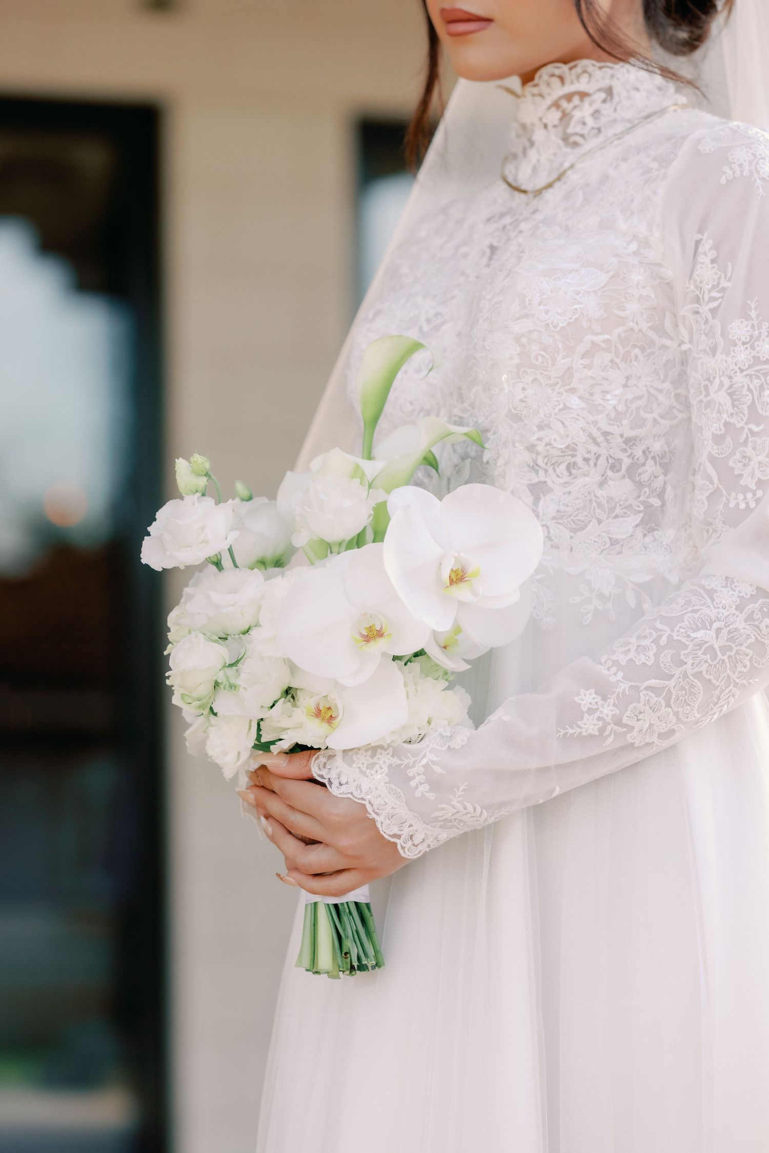 Bride in white lace long-sleeve wedding dress holding elegant bouquet of white orchids and roses.