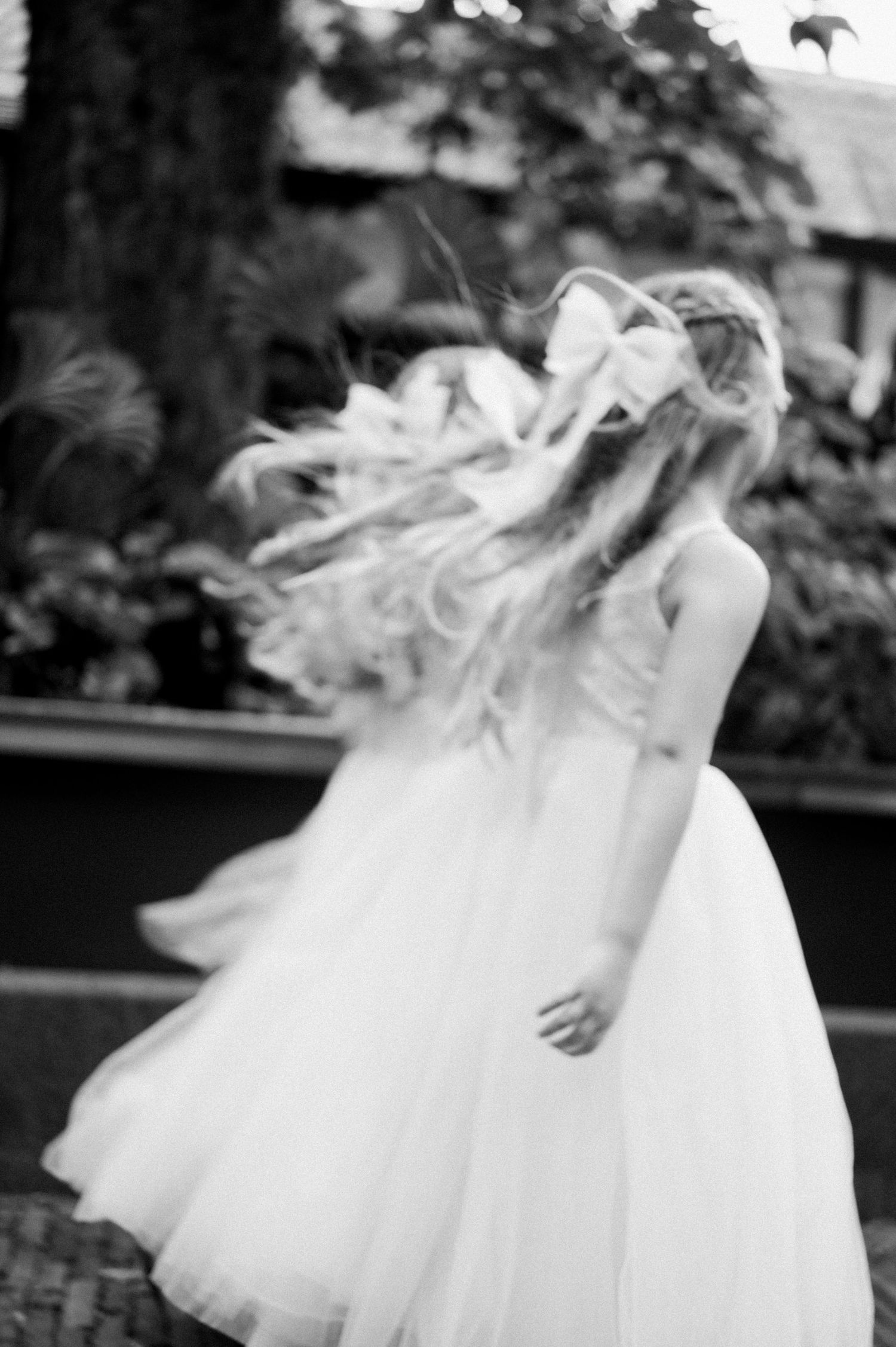 A flowing white dress twirls in motion as long blonde hair catches the wind in this black and white photograph.