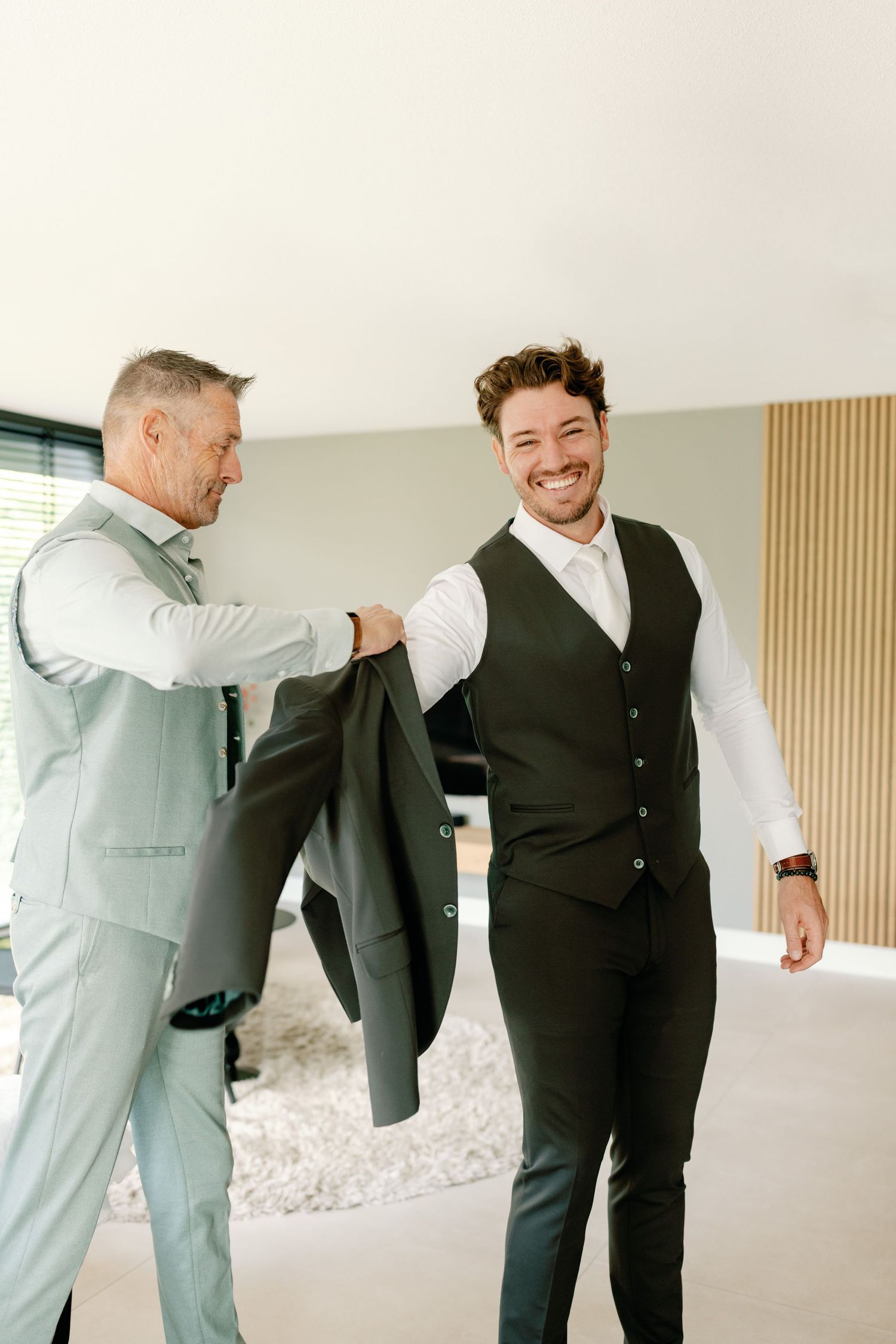 Two people in formal attire embrace in a bright indoor space during what appears to be a special occasion.