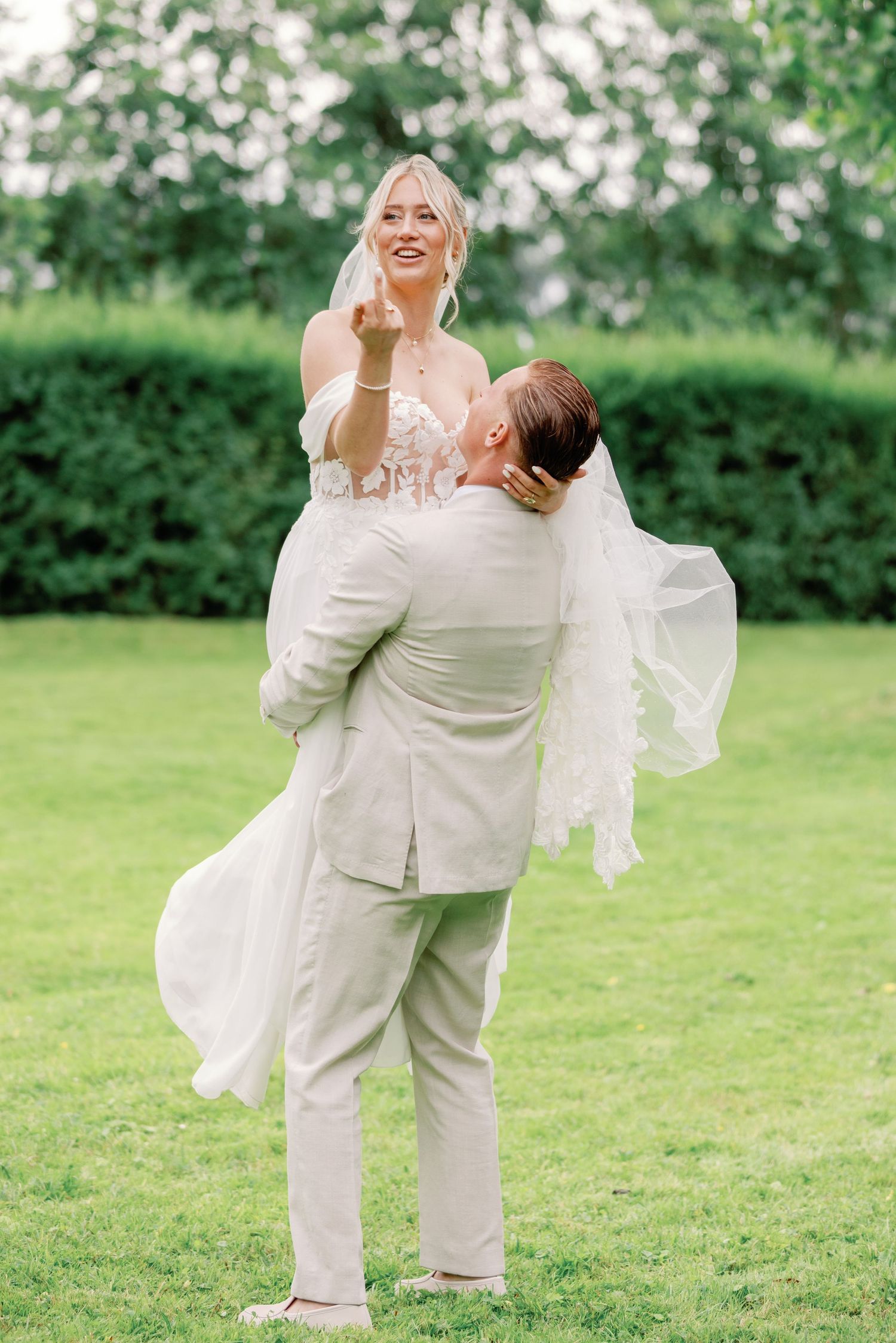 A couple in white attire dances and twirls joyfully on a green lawn during their wedding celebration.