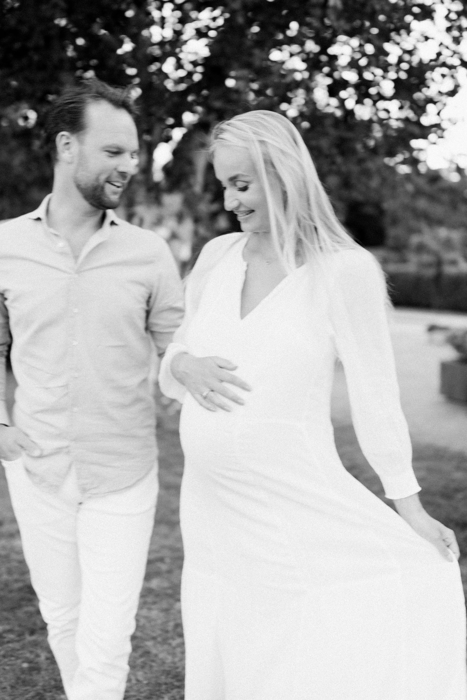 Couple in all white outfits share joyful moment outdoors.
