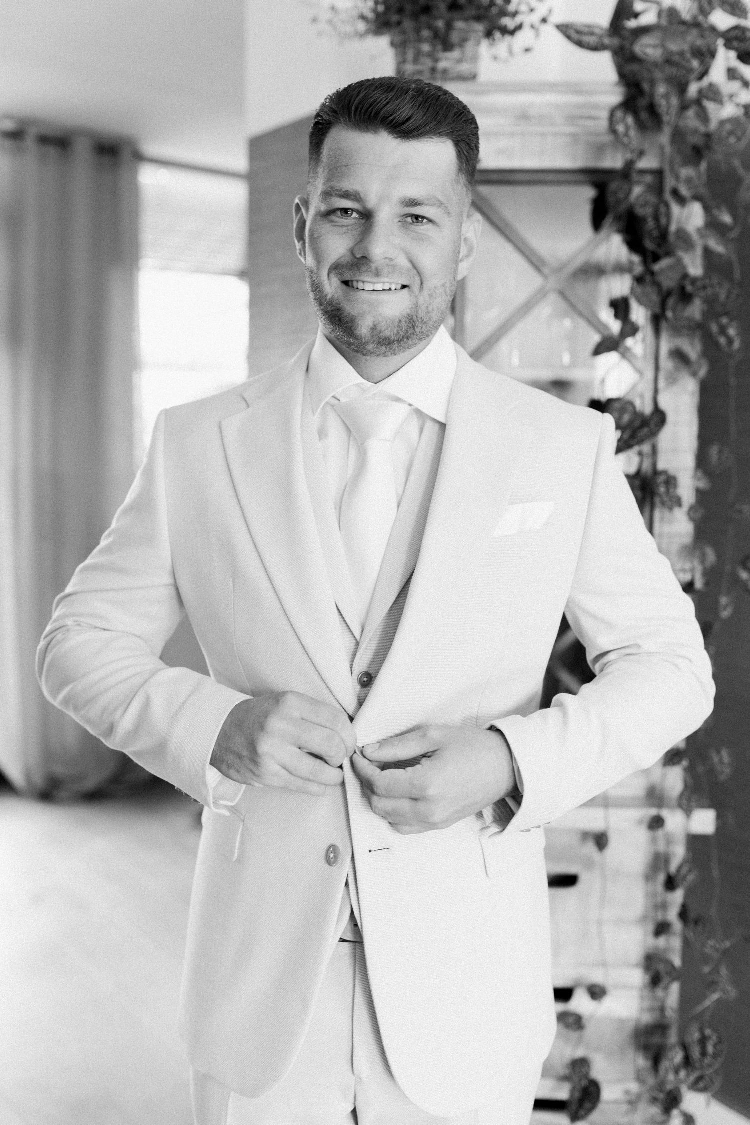 A groom in a crisp white suit and tie smiling at the camera.