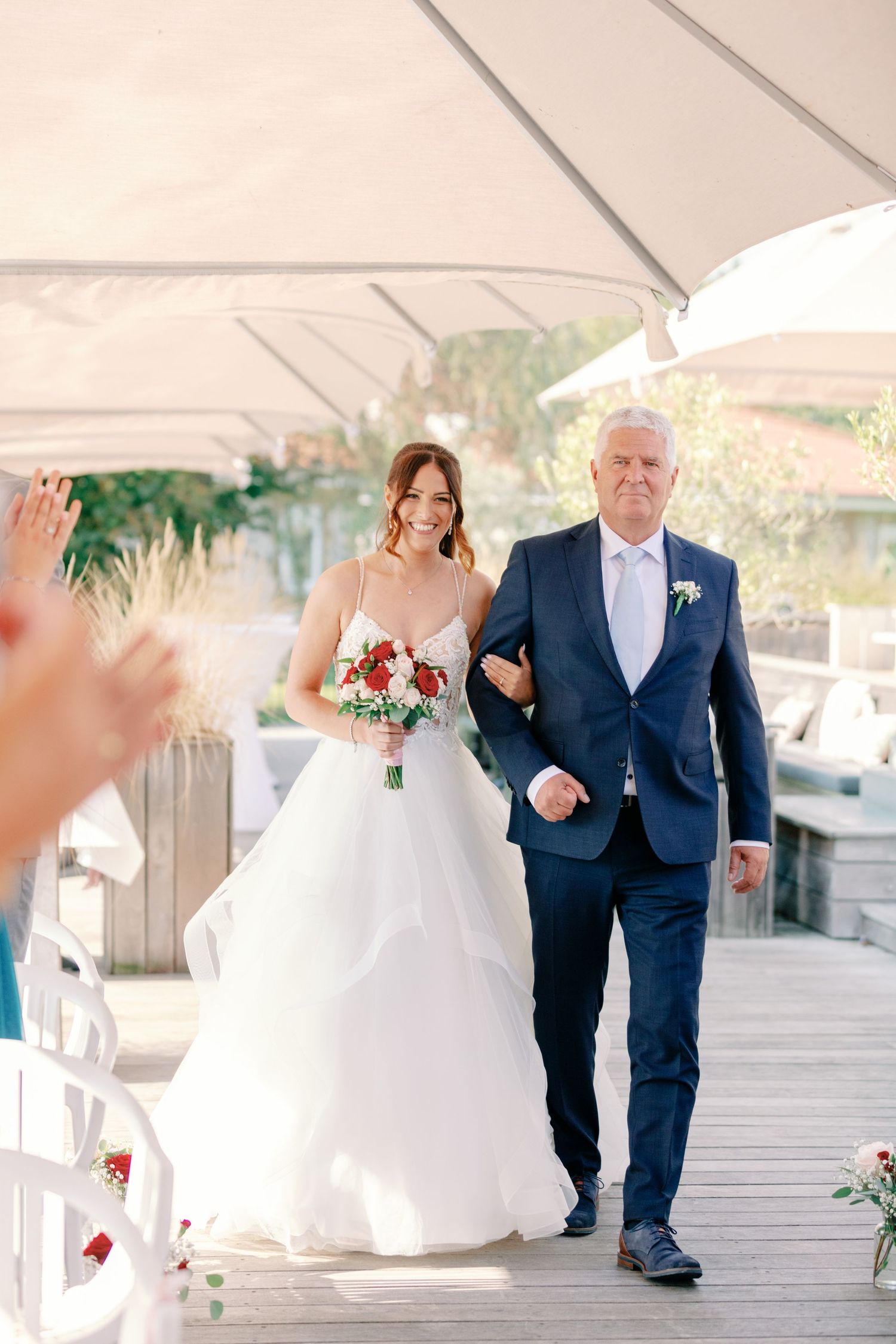 A bride in a white gown walks down a covered walkway with her escort in a navy suit.