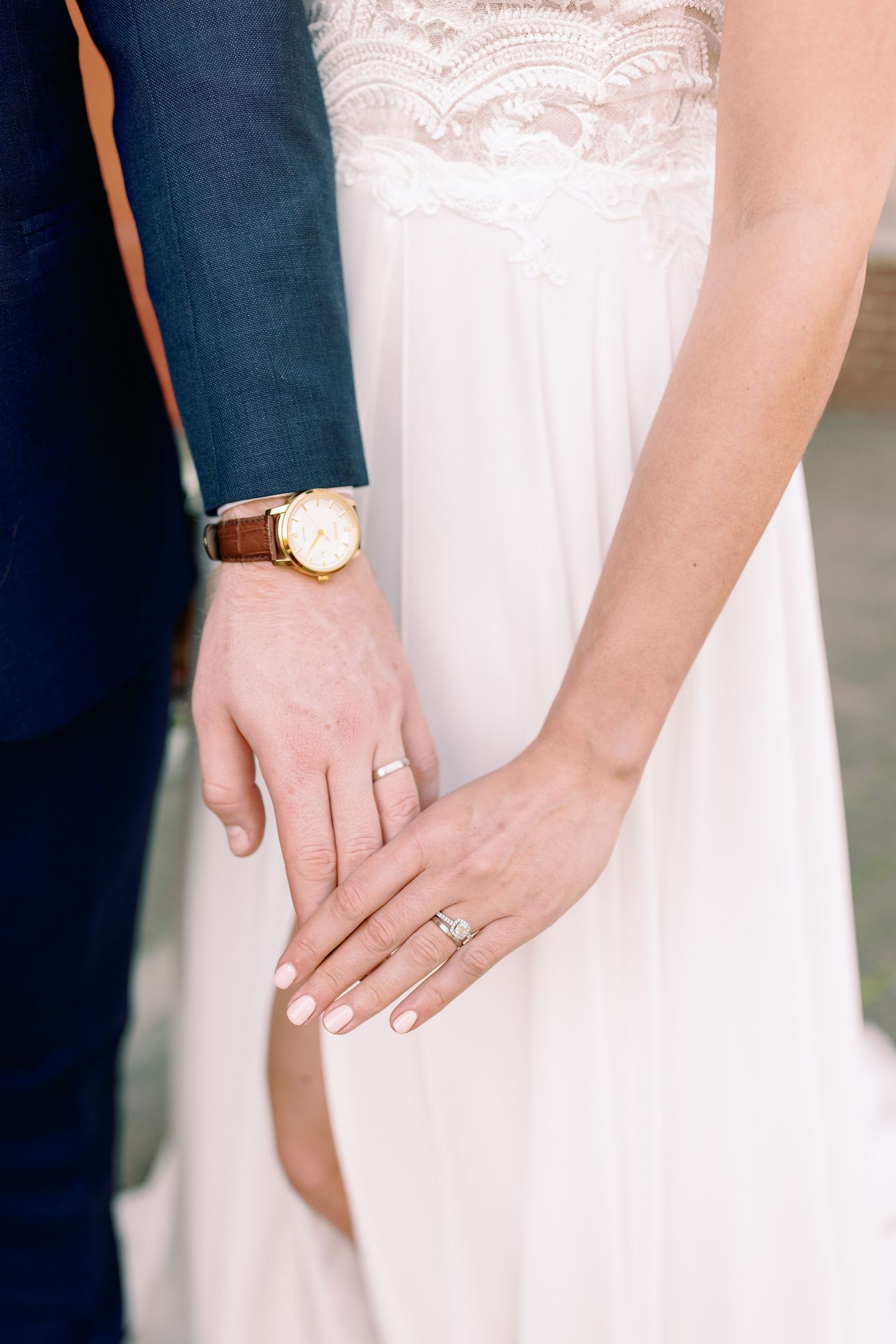 Close-up detail shots of wedding rings and hands against white lace dress and navy suit.