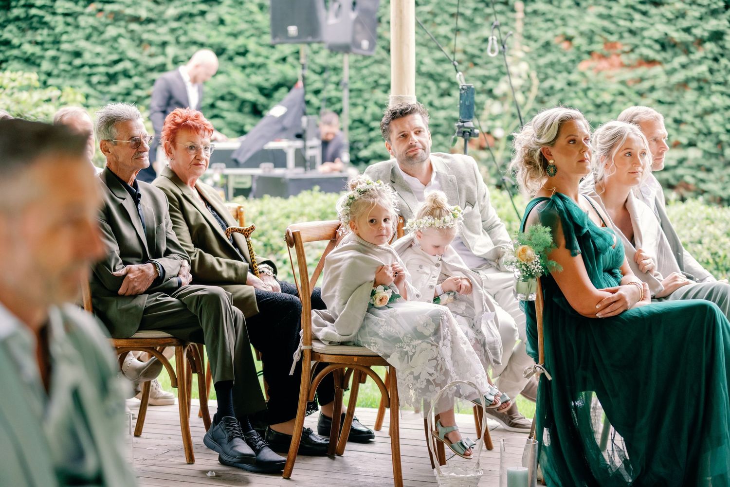 Wedding guests seated outdoors at a garden ceremony with lush greenery in the background.