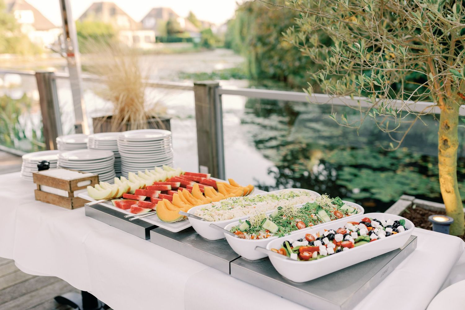 Elegant outdoor wedding reception buffet tables with fresh salads and appetizers displayed under trees.