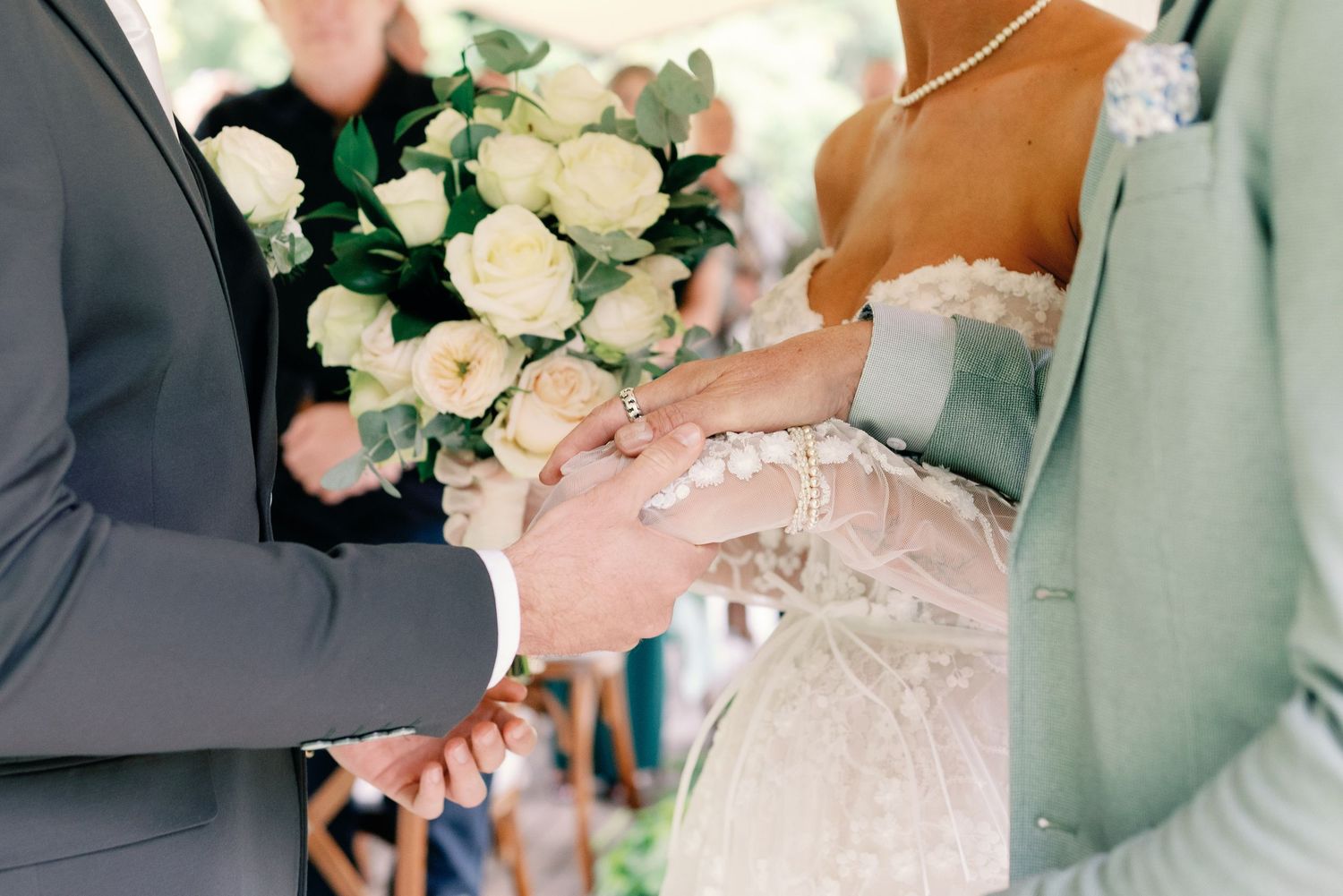 A close-up view of a wedding bouquet with white roses being held during an outdoor ceremony.