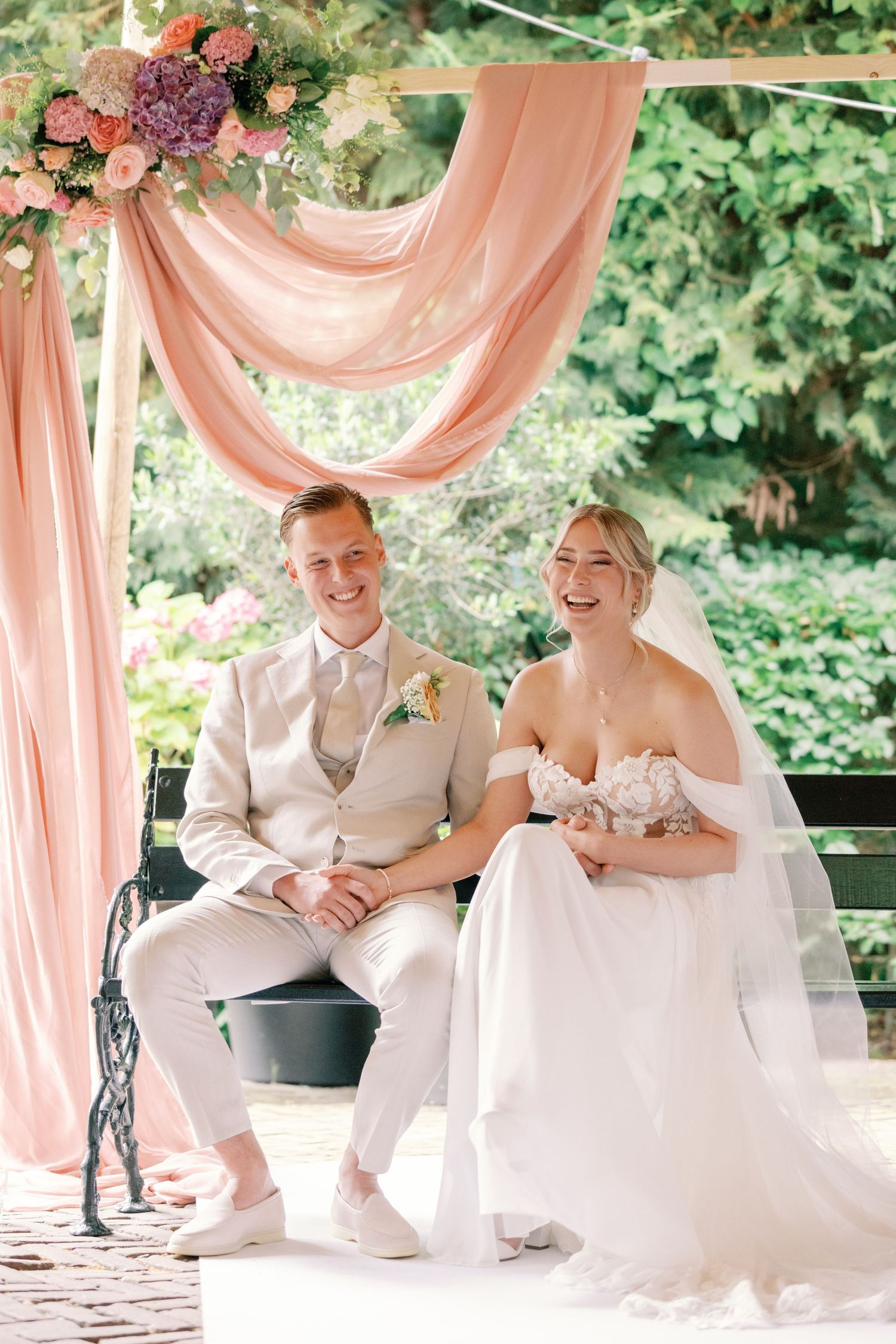 A couple shares a joyful moment together under elegant pink drapery at an outdoor wedding venue.