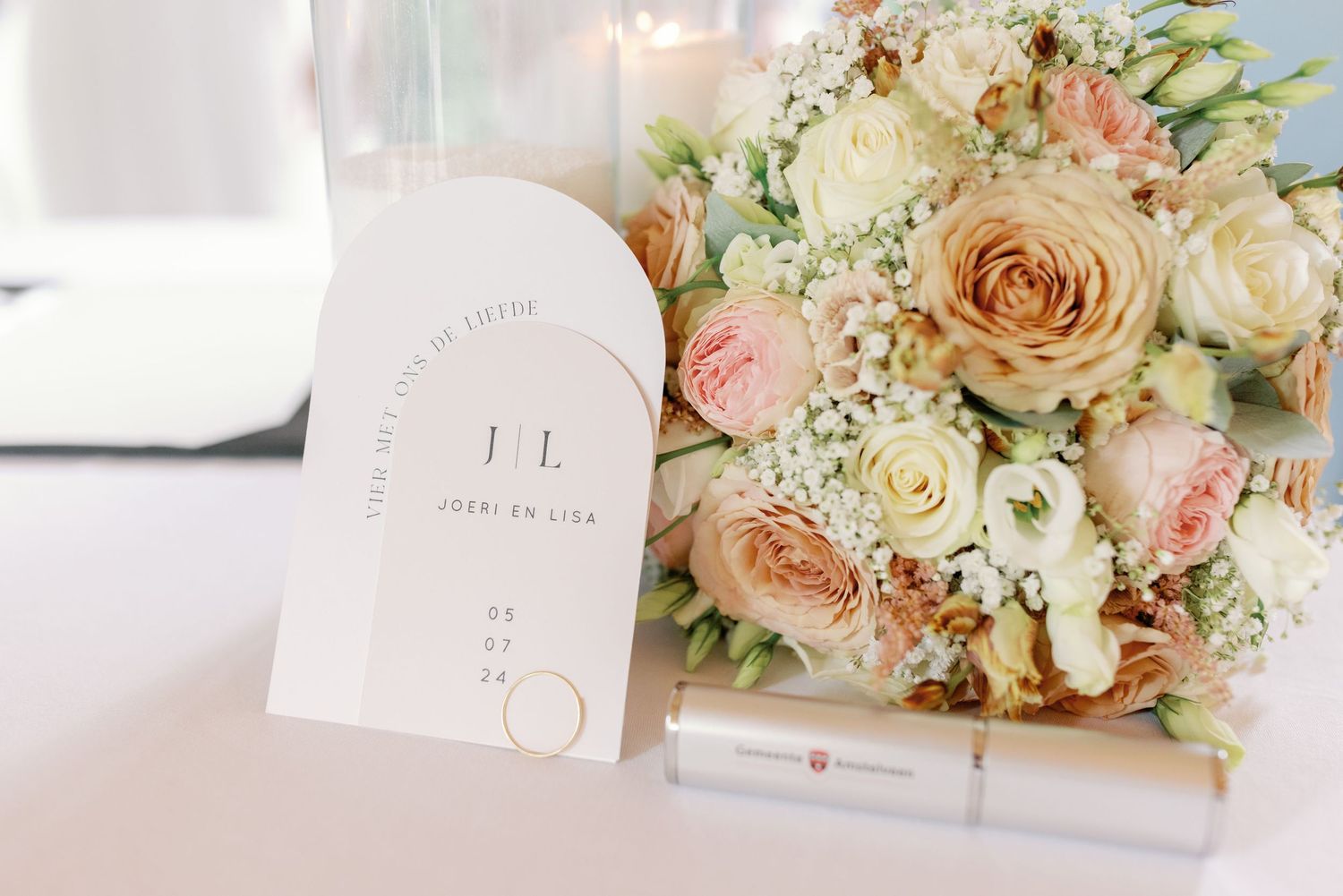 Elegant wedding invitation card displayed next to a romantic bouquet of peach and white roses with baby's breath.