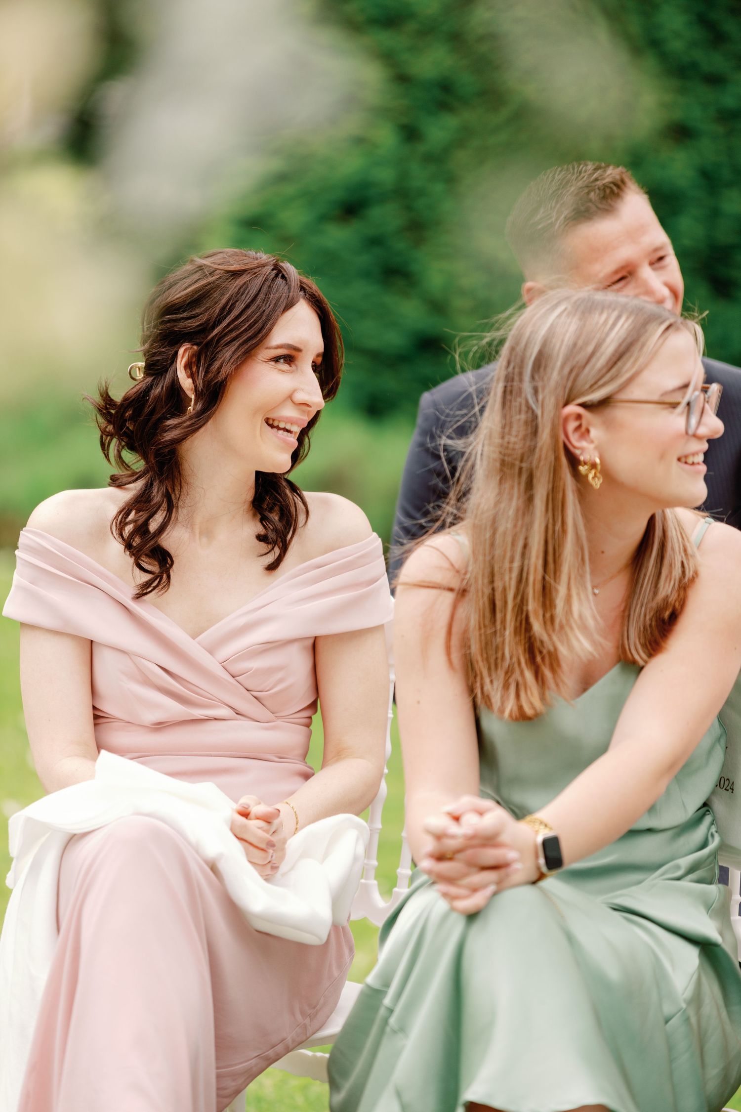 Two people in pink and mint green dresses share a candid laughing moment during a formal event outdoors.