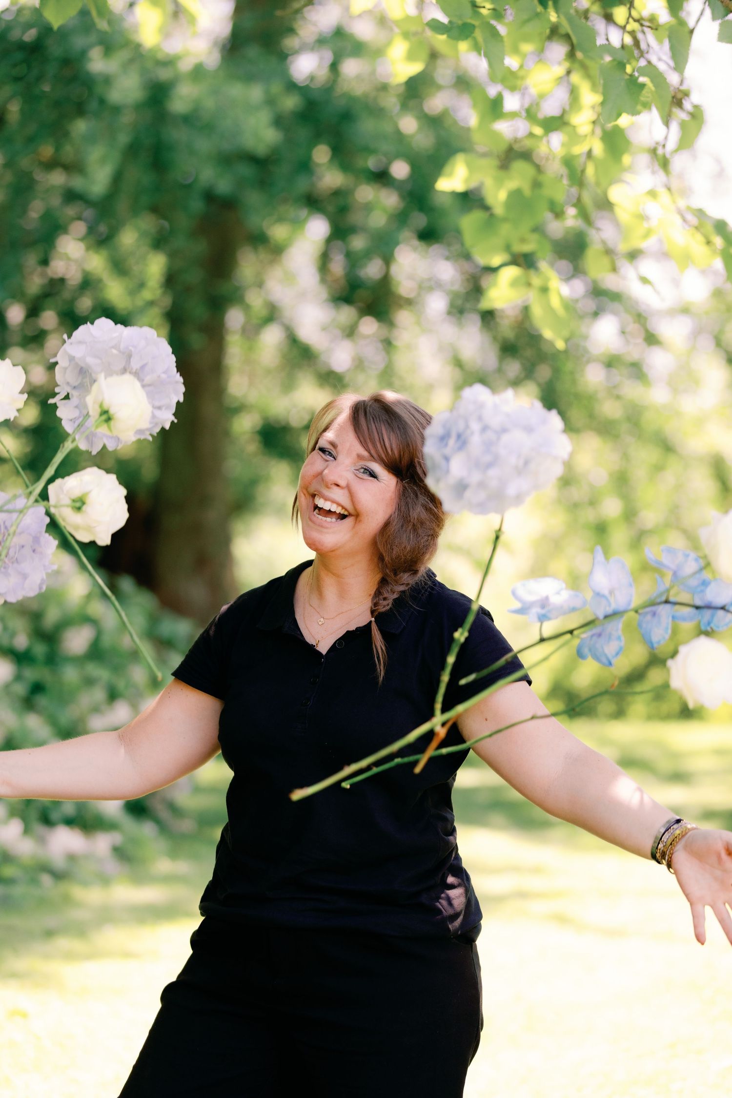 Joyful woman in black outfit holding white flowers outdoors in a lush green garden setting.